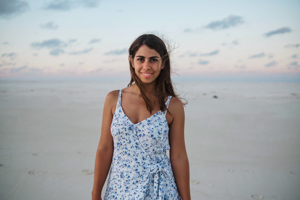 A young woman stands smiling on a white sandy beach