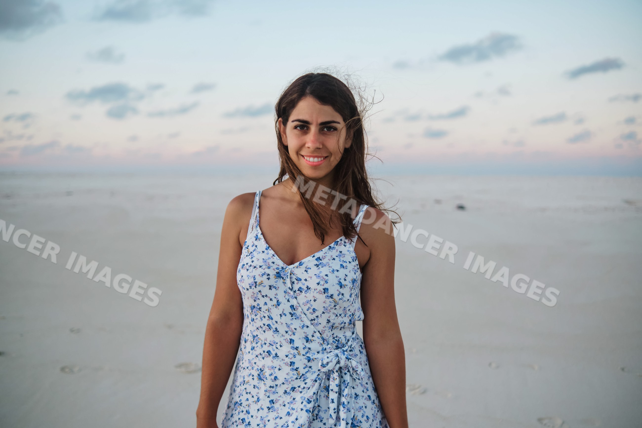A young woman stands smiling on a white sandy beach