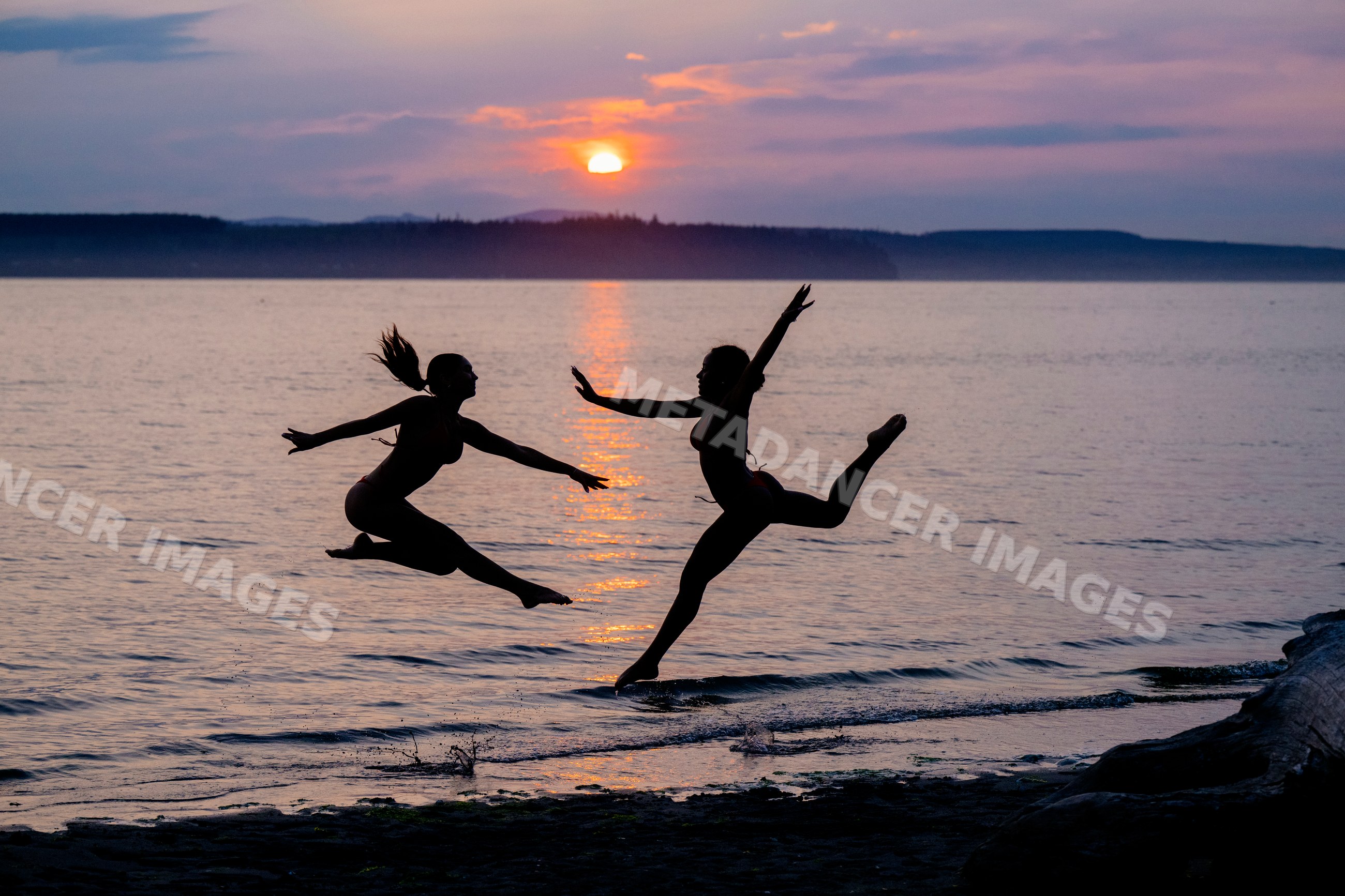 Two women perform partner acrobatics jumping on the beach at sunset