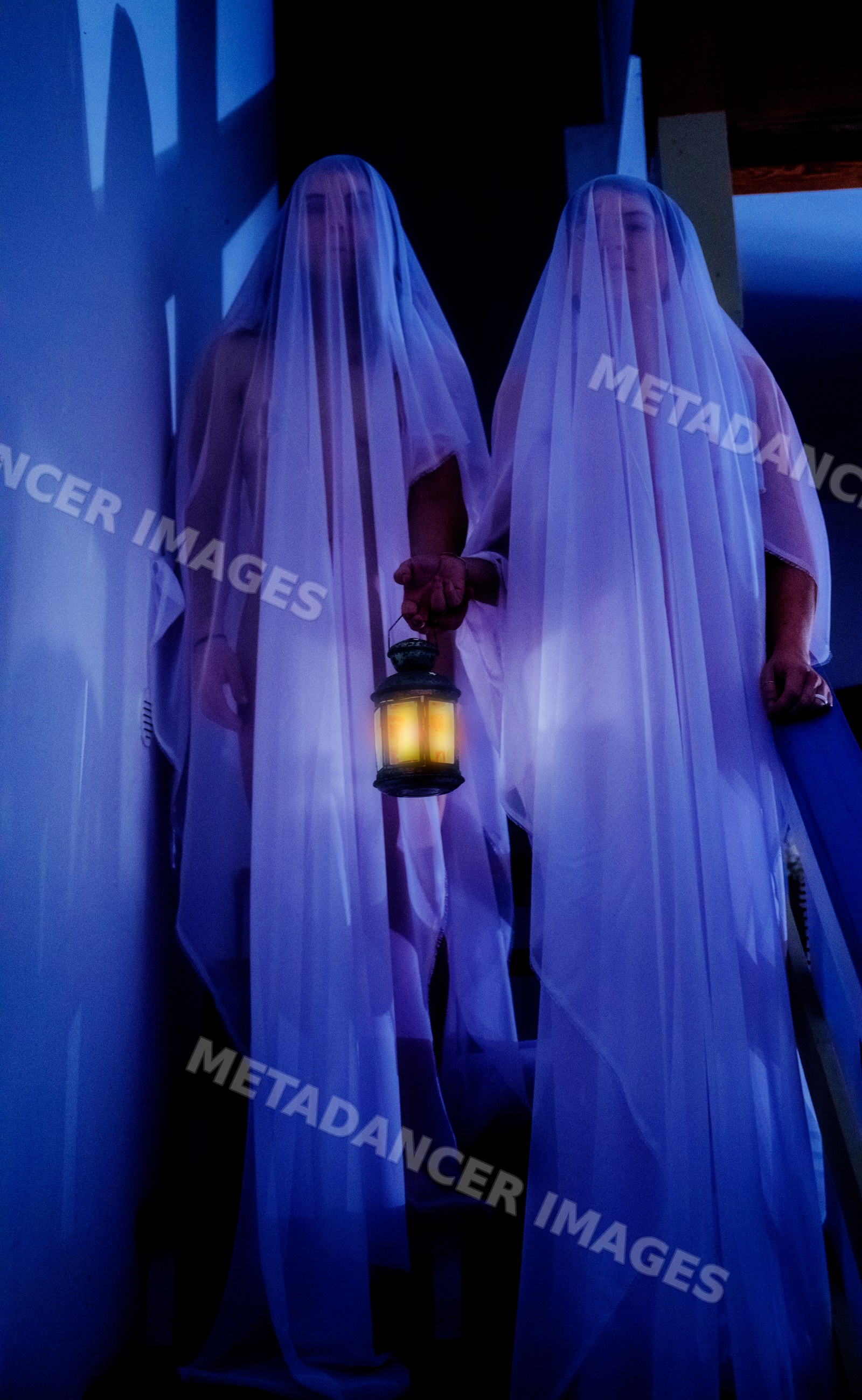 White people dressed as ghosts holding lantern on dark staircase