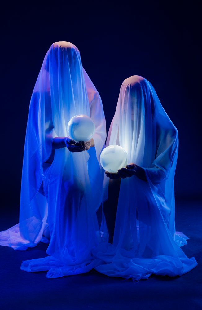 Two ghostly figures holding illuminated crystal balls in blue light