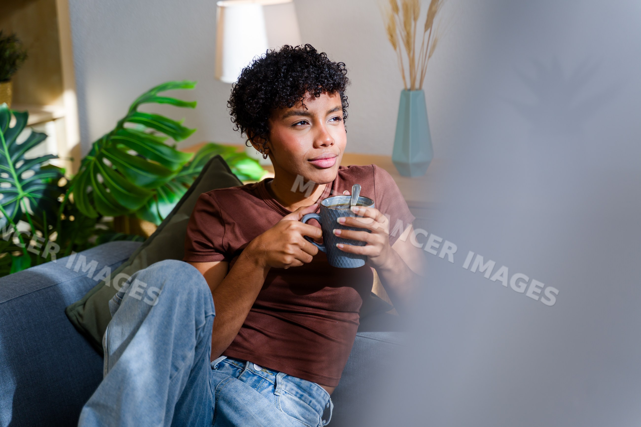 African American woman holding mug and relaxing on sofa