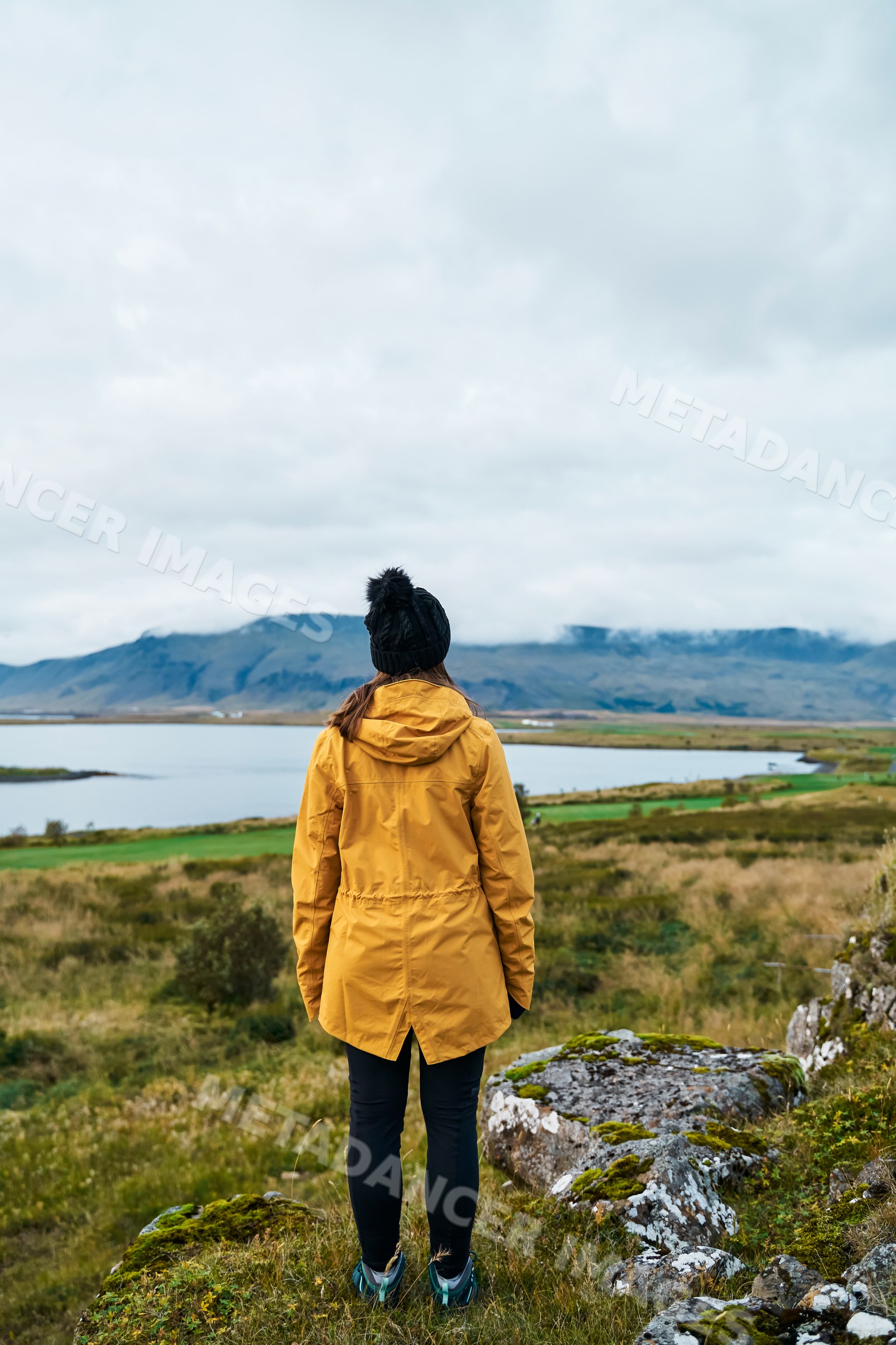 A white woman stands overlooking a scenic lake and mountain landscape