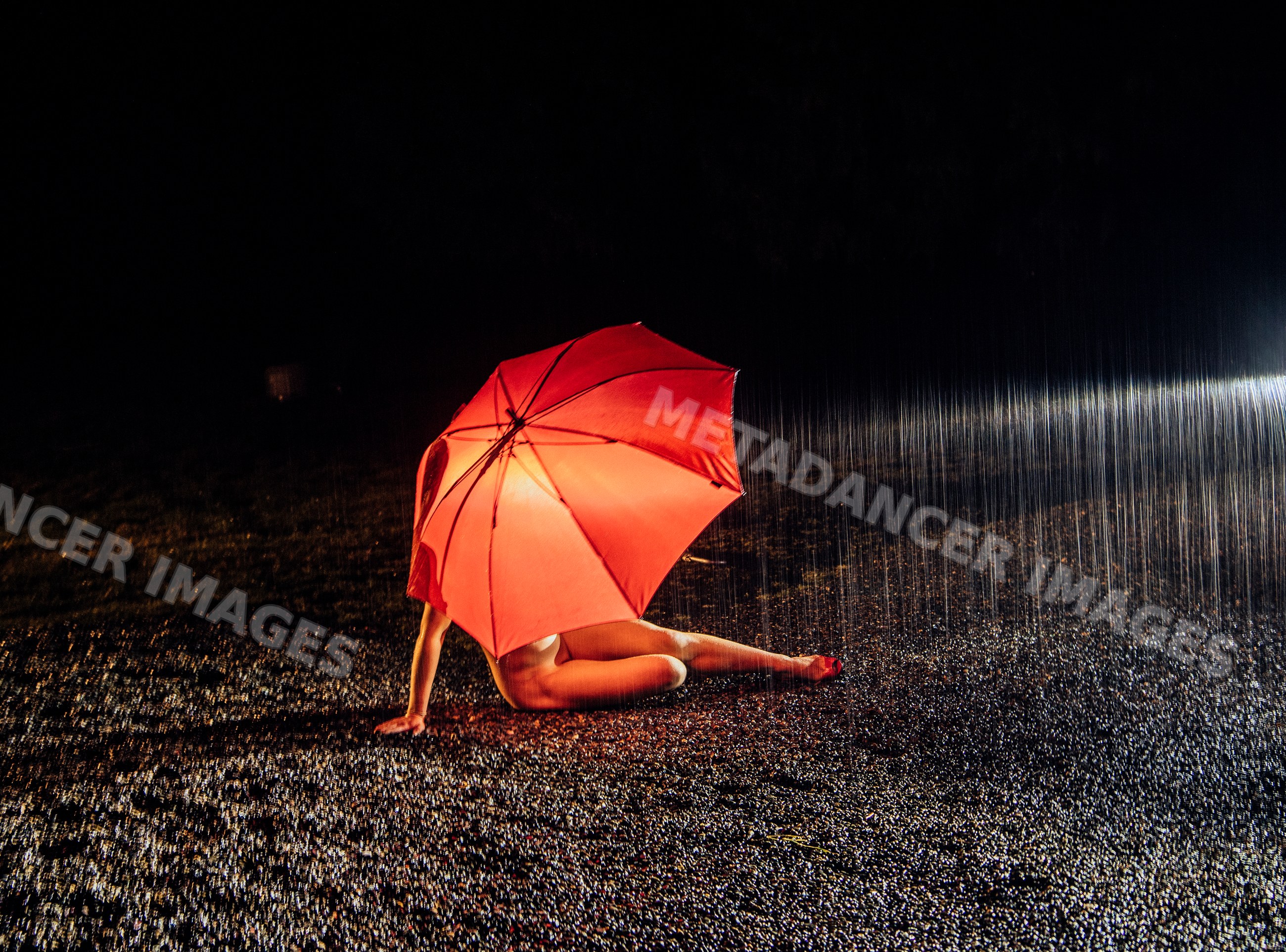 White person sitting with red umbrella in rain at night