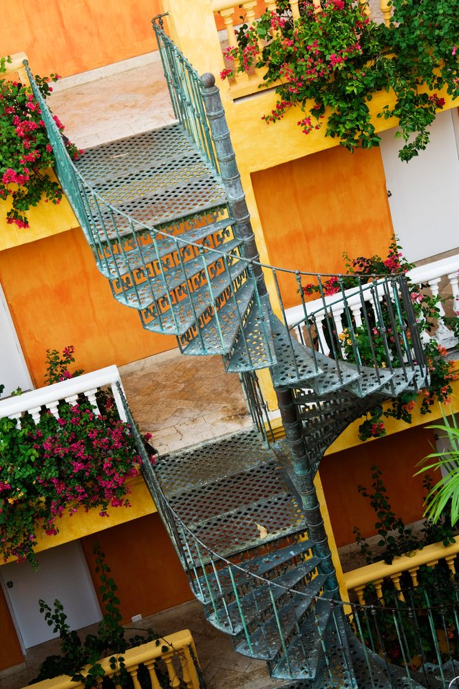 Spiral green metal staircase with climbing flowers on yellow walls