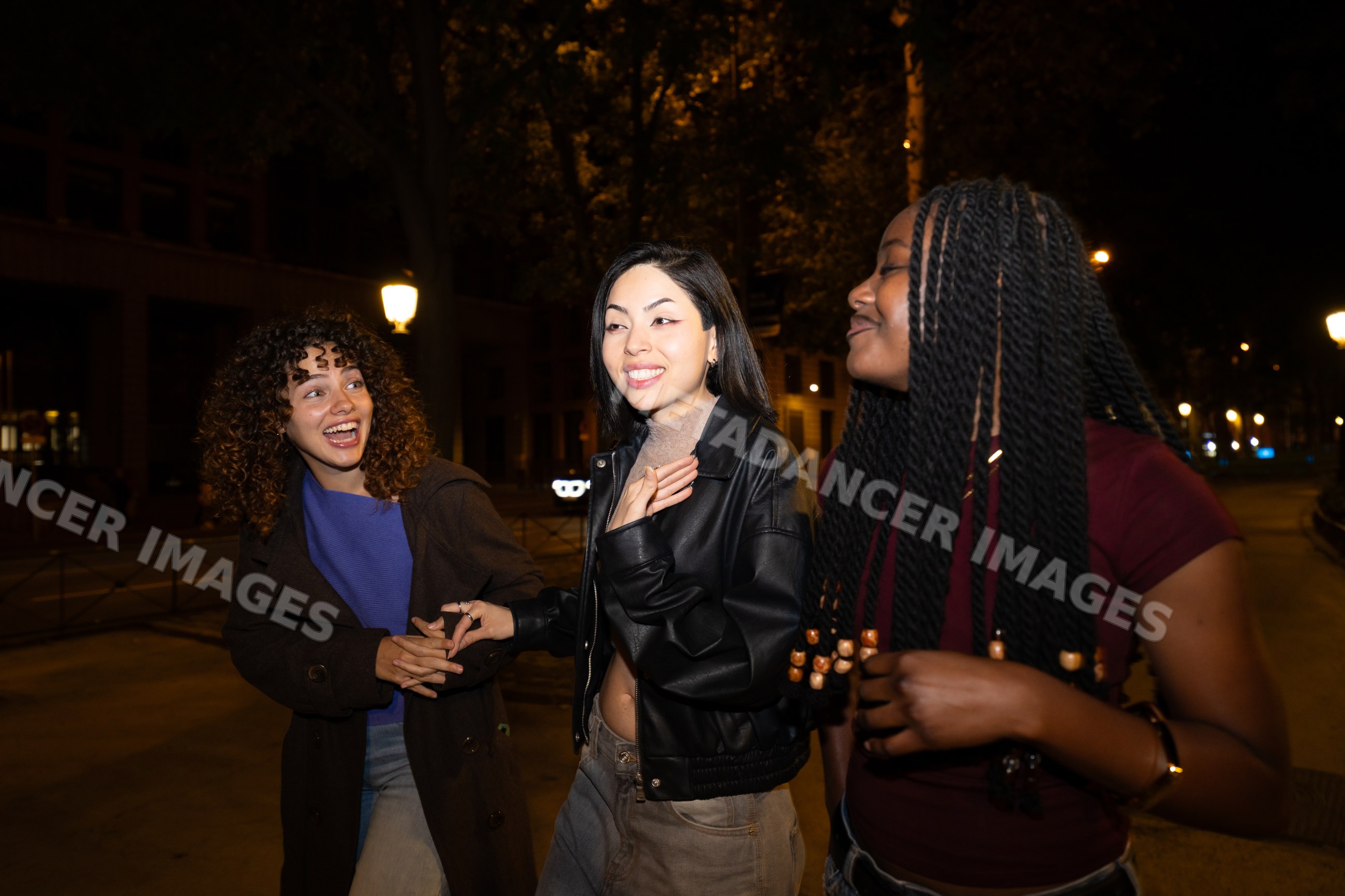 Three Hispanic, white and Black women socializing at night on a street