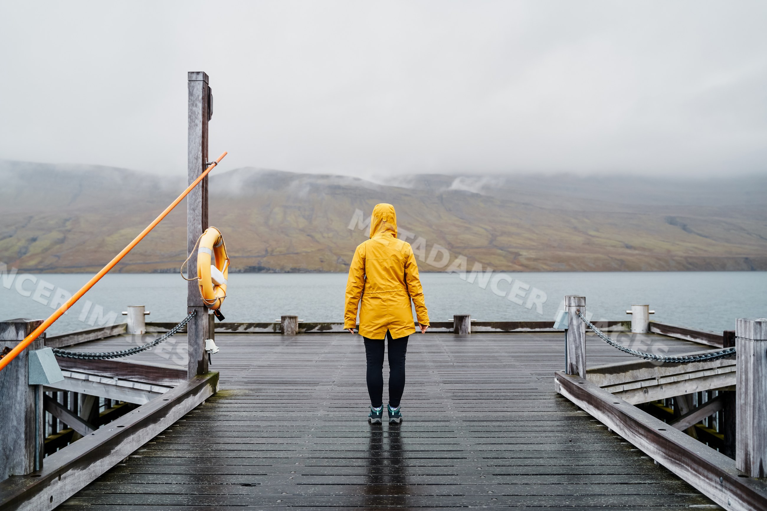 A white person in a yellow raincoat stands on a wooden pier