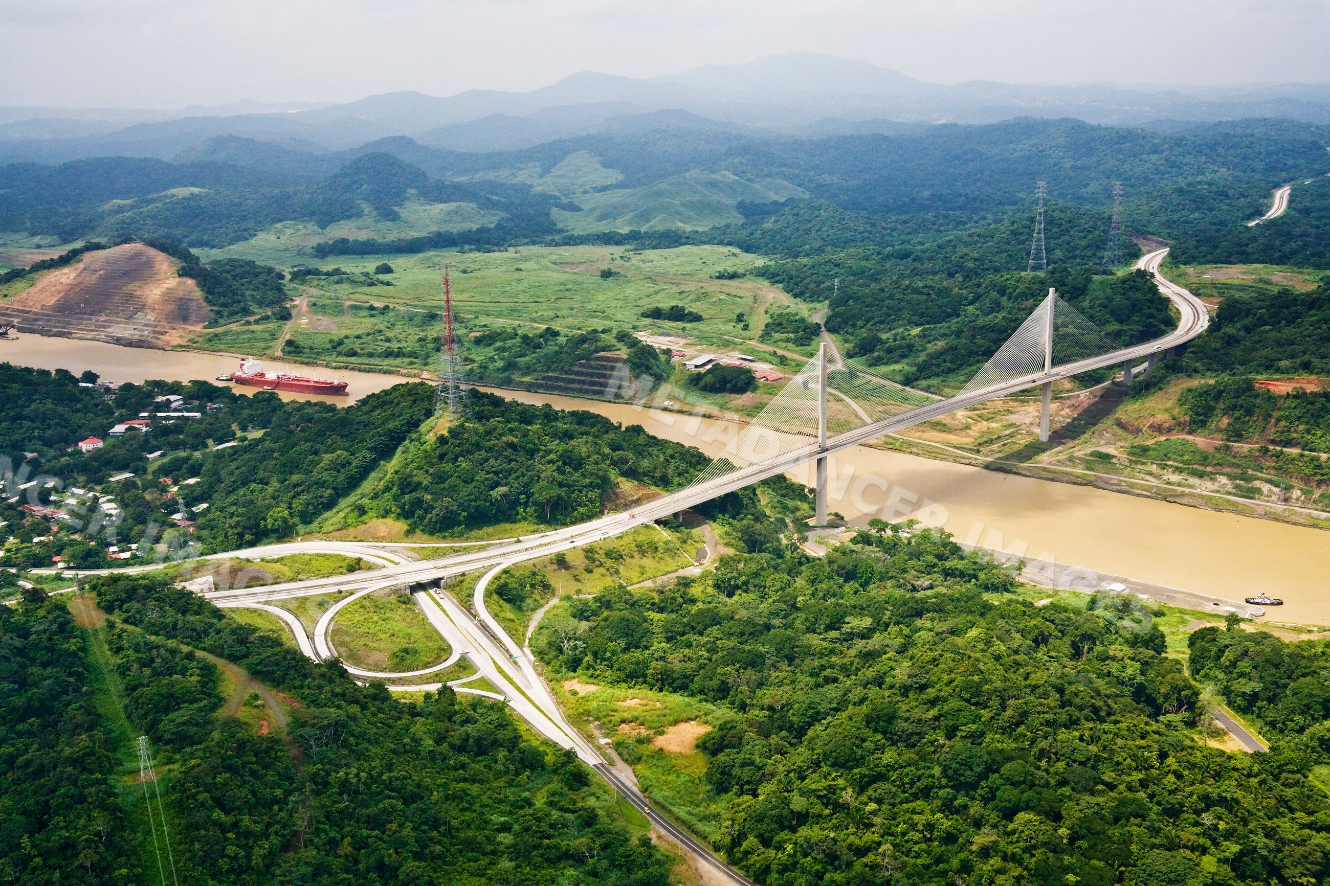 Panama canal bridge with cargo ship passing beneath and green hilly