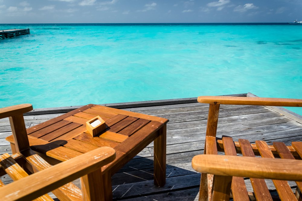 Wooden deck with chairs by turquoise ocean water and pier
