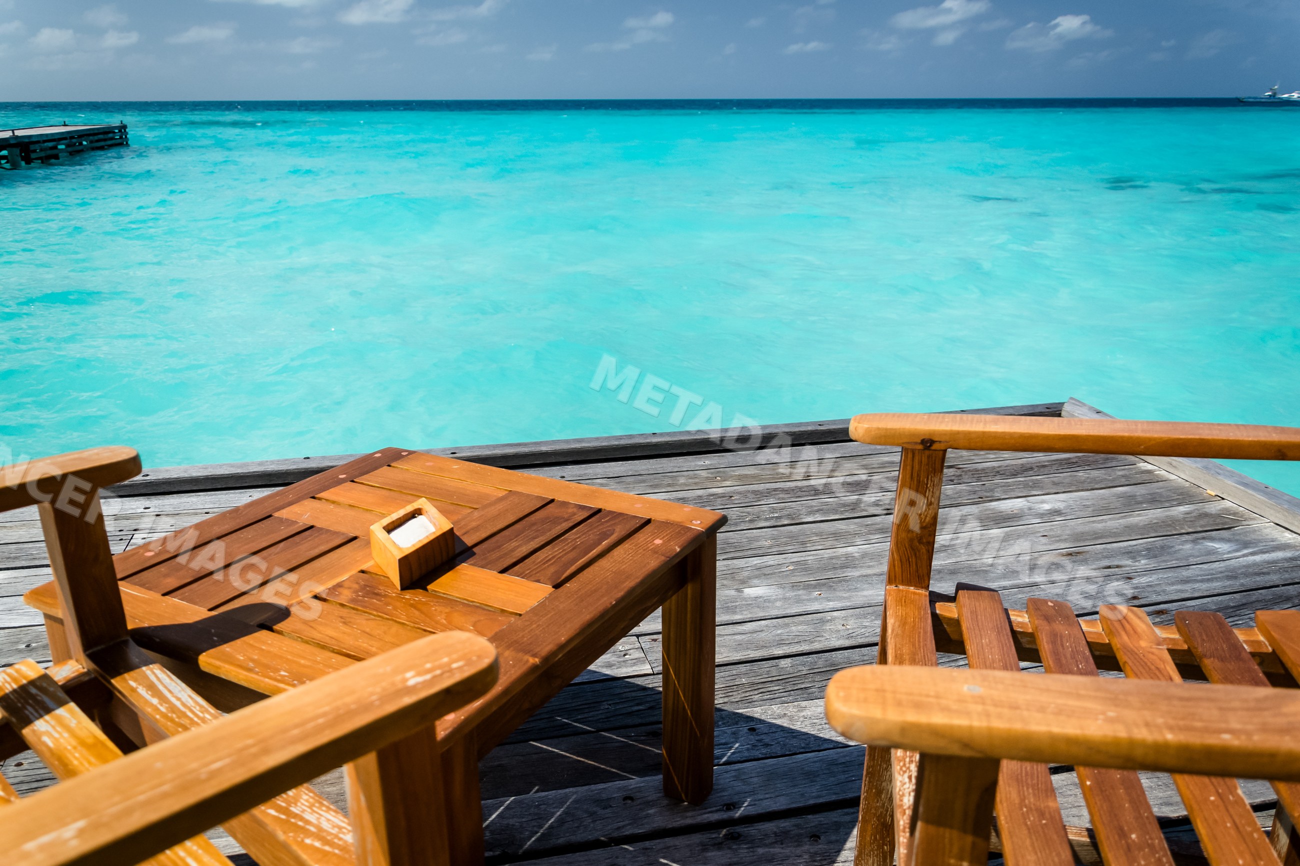 Wooden deck with chairs by turquoise ocean water and pier