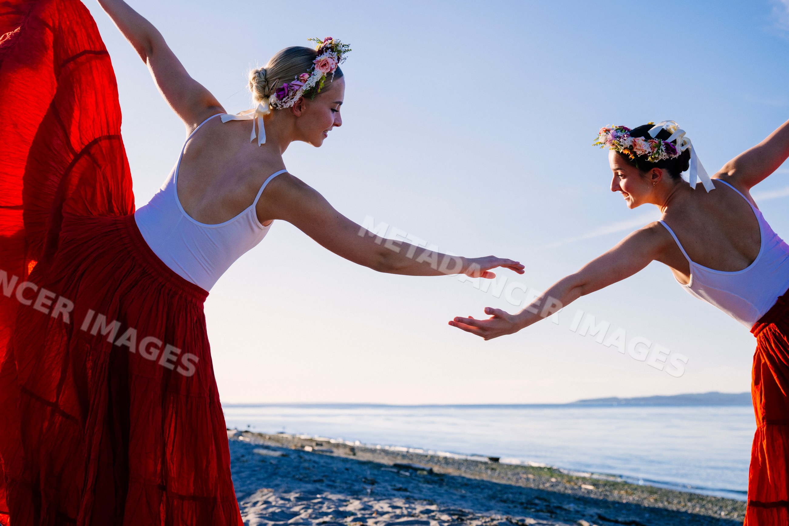 Two white women practicing partner acrobatics yoga on a beach