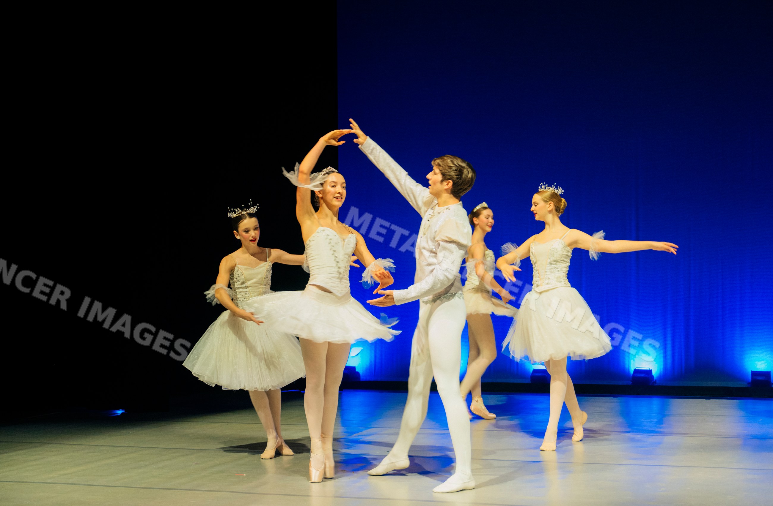 Ballet dancers perform a classical routine on stage with blue lighting