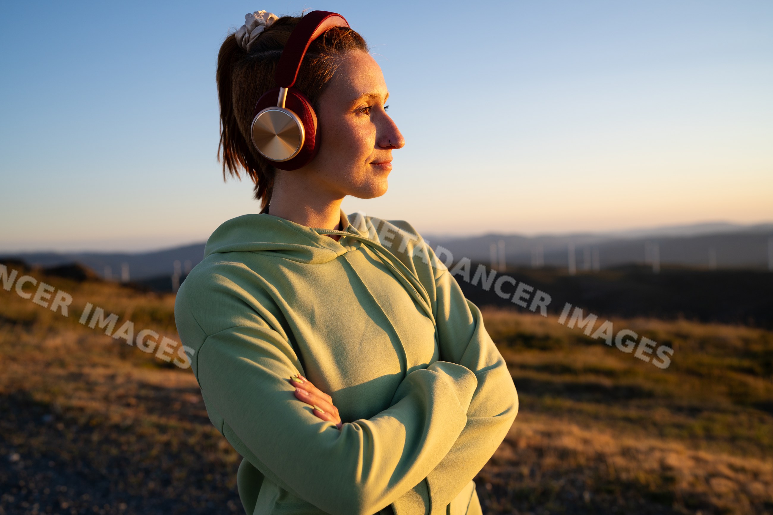 A white woman wearing headphones enjoys the sunset outdoors