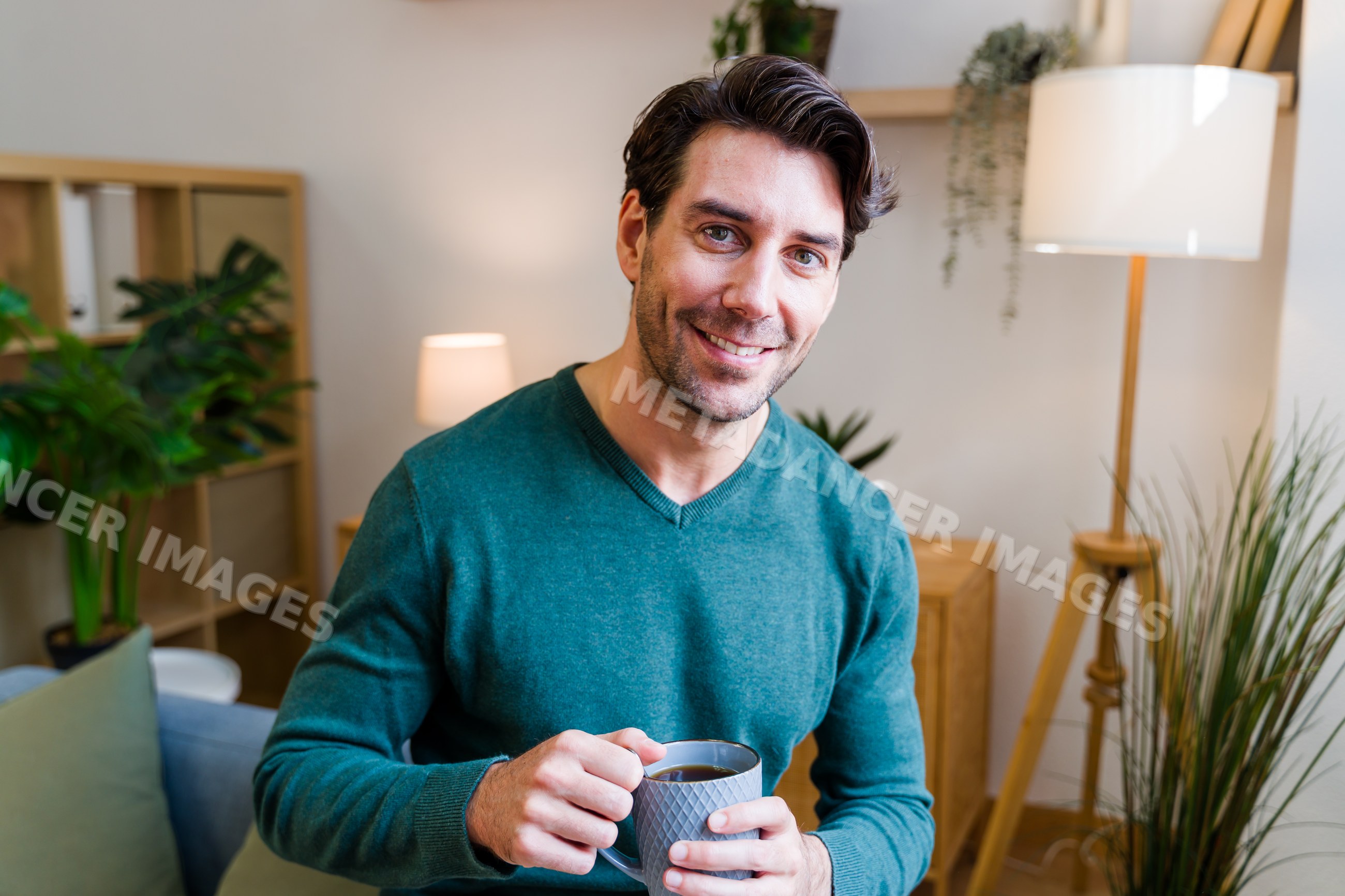 White man holding gray ceramic mug smiling indoors in cozy living room