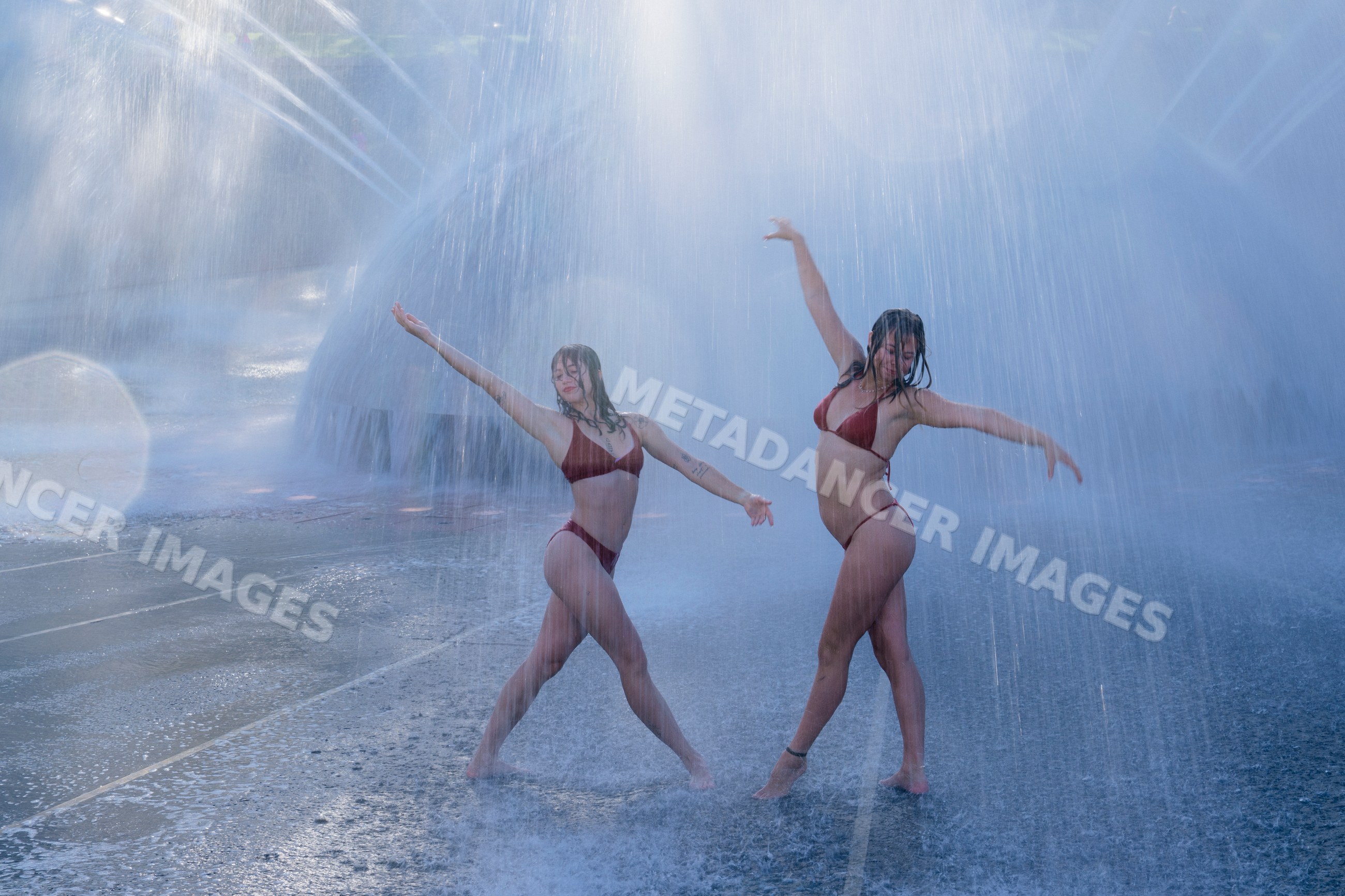 Two white women dancing under outdoor fountain water spray