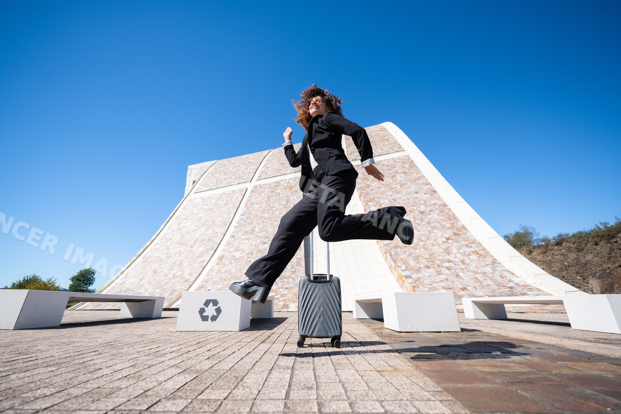 White female professional jumping with luggage