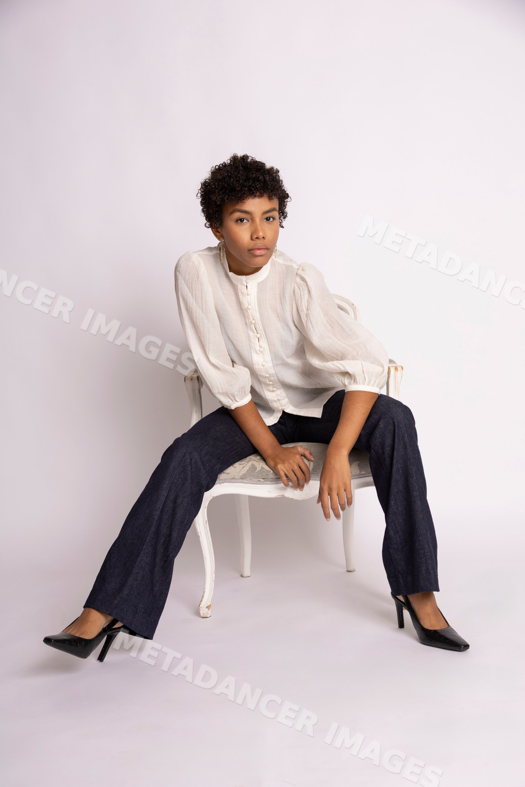 Hispanic woman sitting on antique chair wearing white blouse and denim