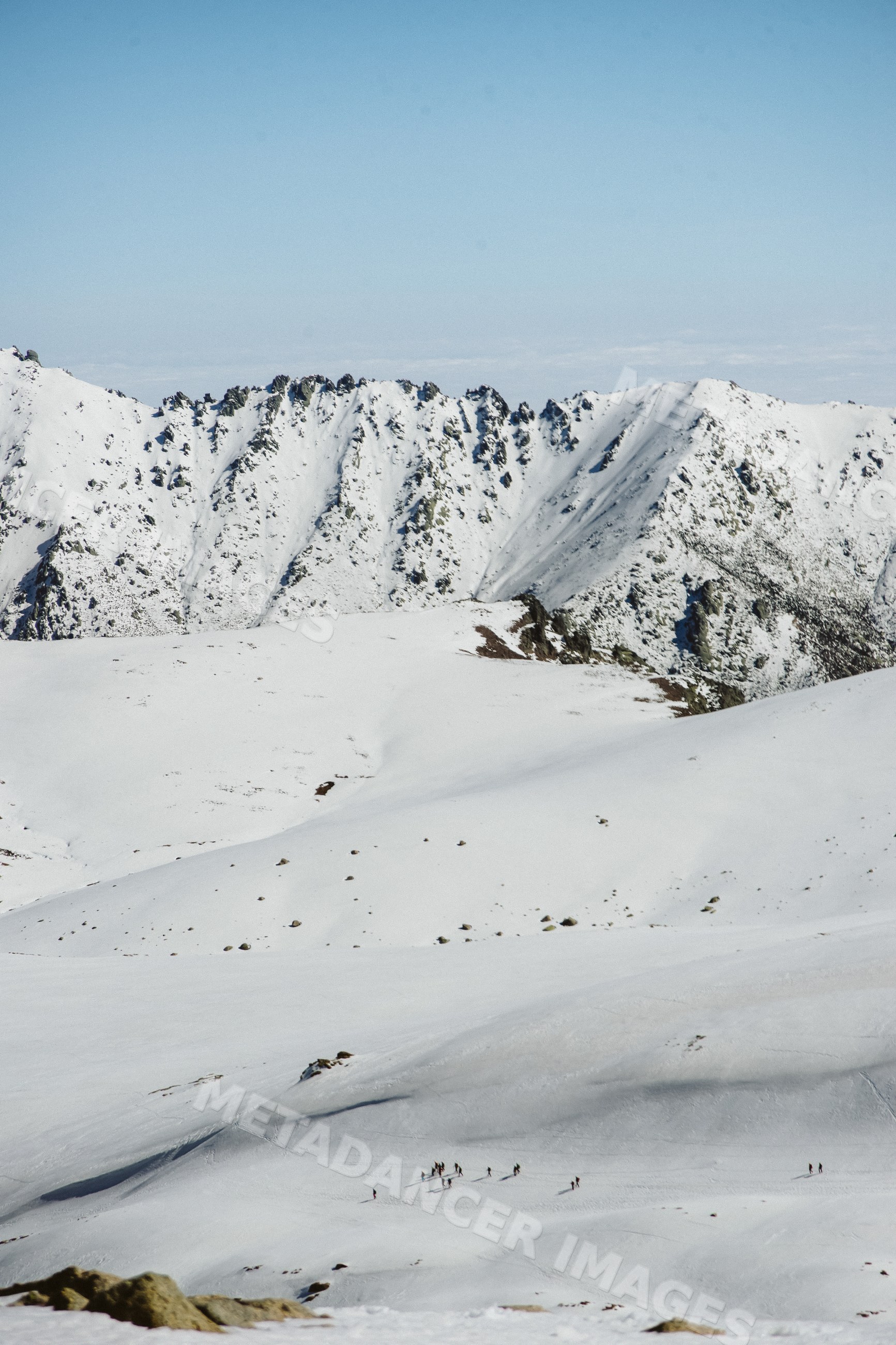 Mountaineering group hiking snowy mountains with rocky peaks
