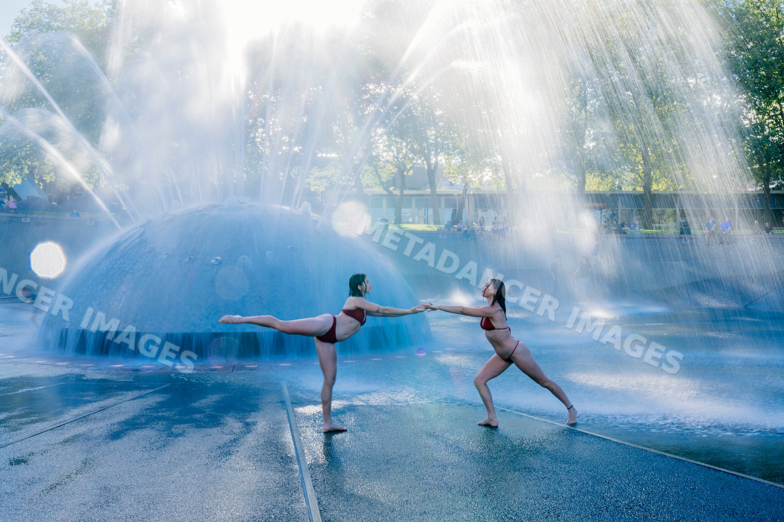 Two white women doing acrobatic yoga poses by an outdoor water