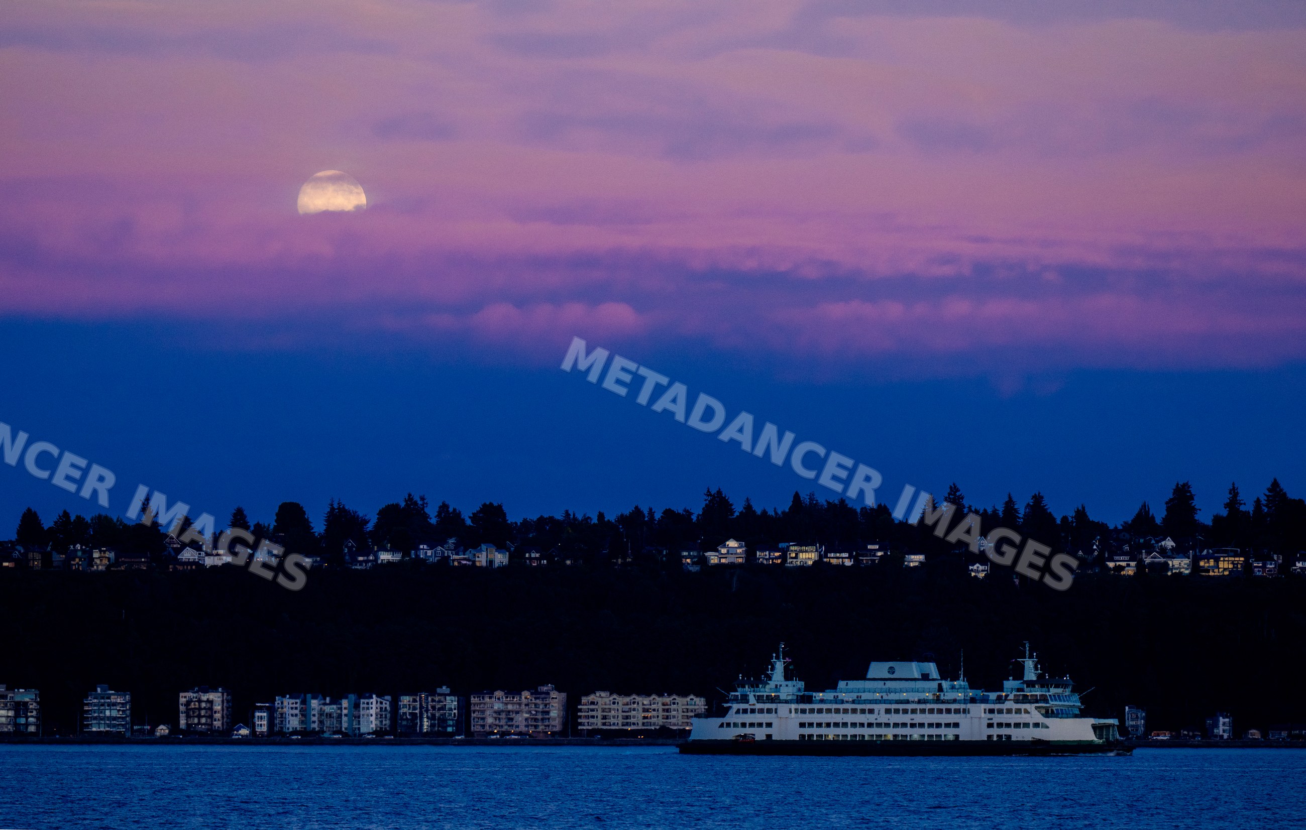 Ferry crossing water with moon rising over coastal residential area