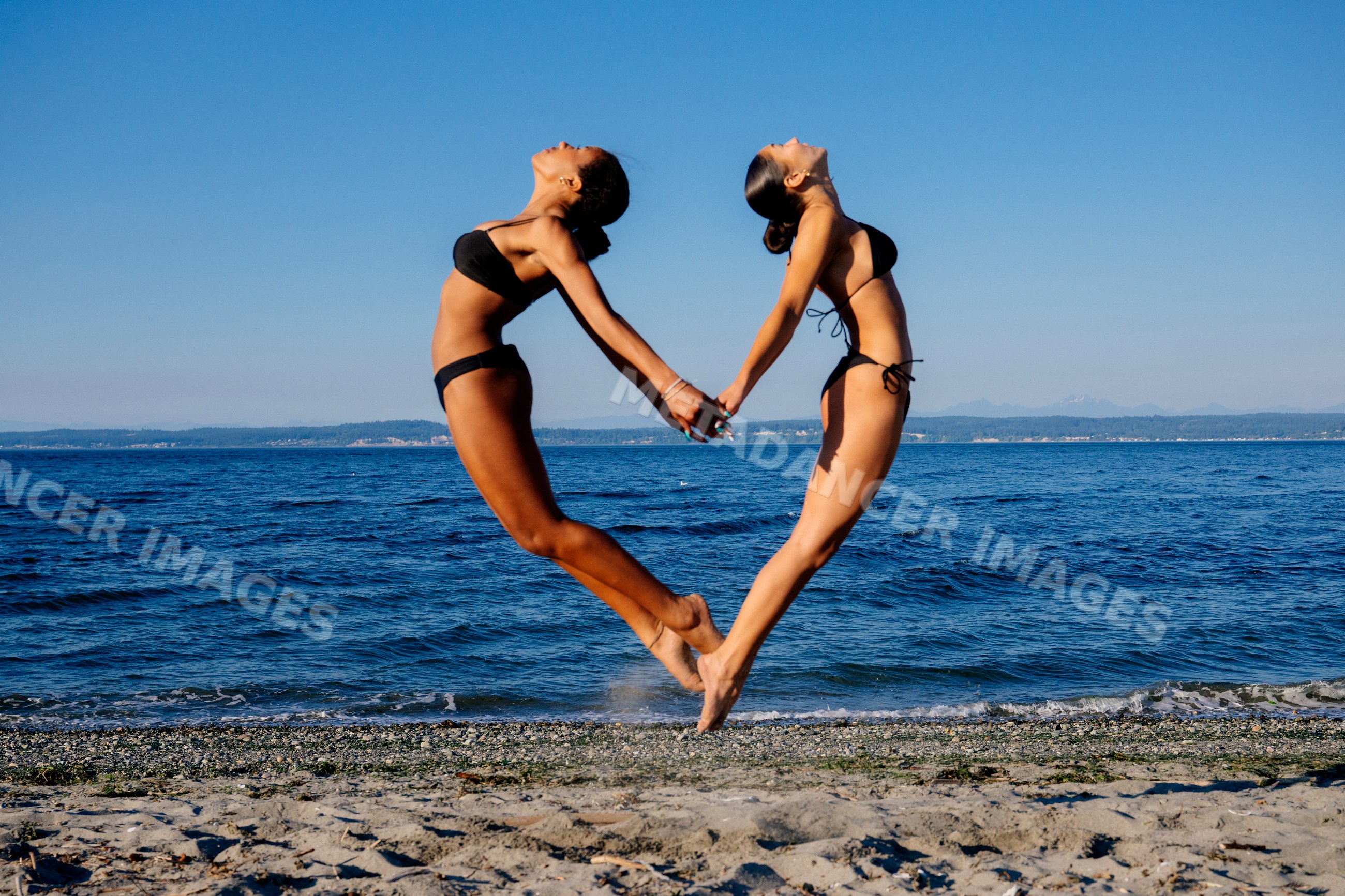 Two women doing acrobatic yoga poses holding hands on a beach