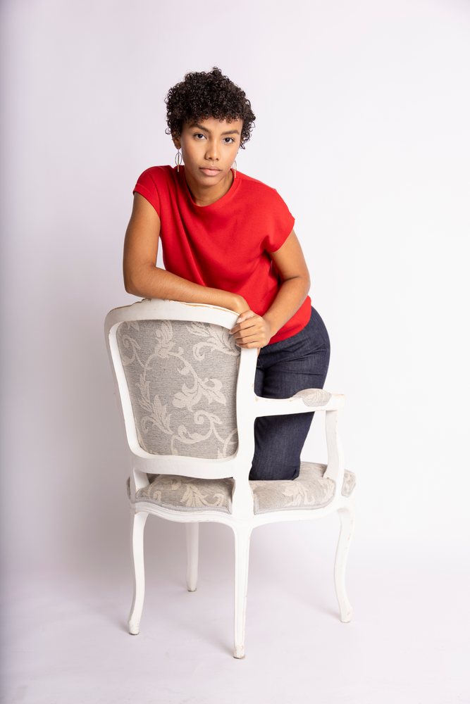 Hispanic woman leaning on a vintage upholstered chair