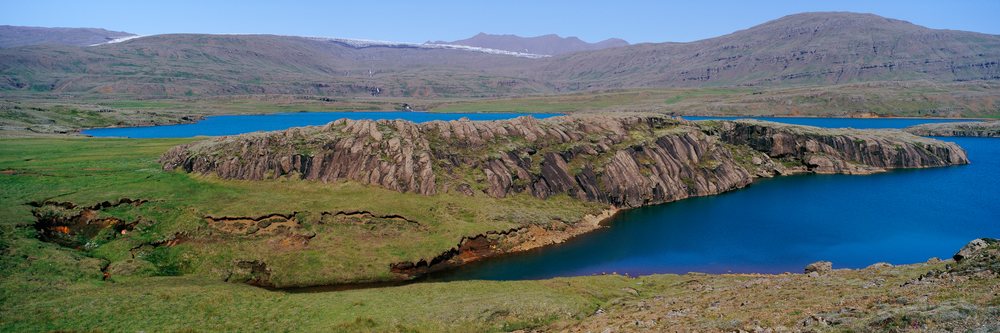 Rock formation beside lake with mountainous and grassy hills landscape