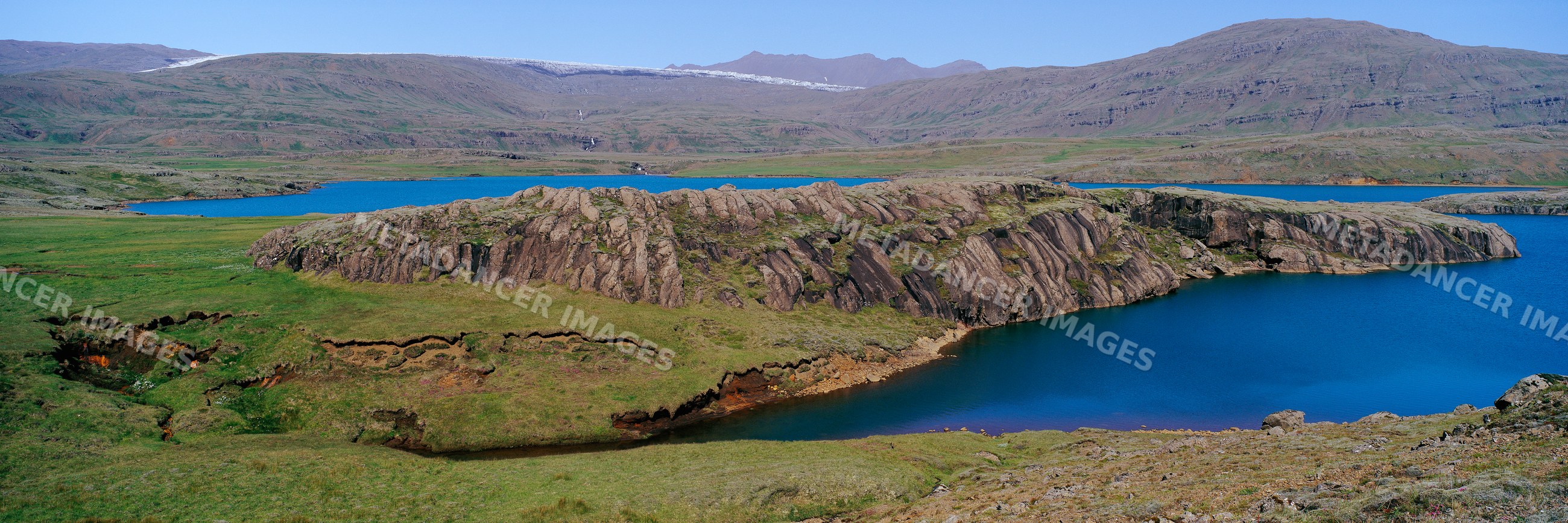 Rock formation beside lake with mountainous and grassy hills landscape