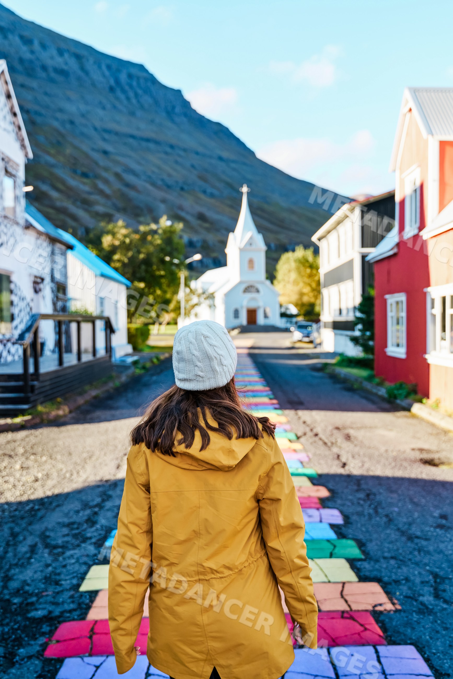 A woman walks along a colorful street path toward a white church