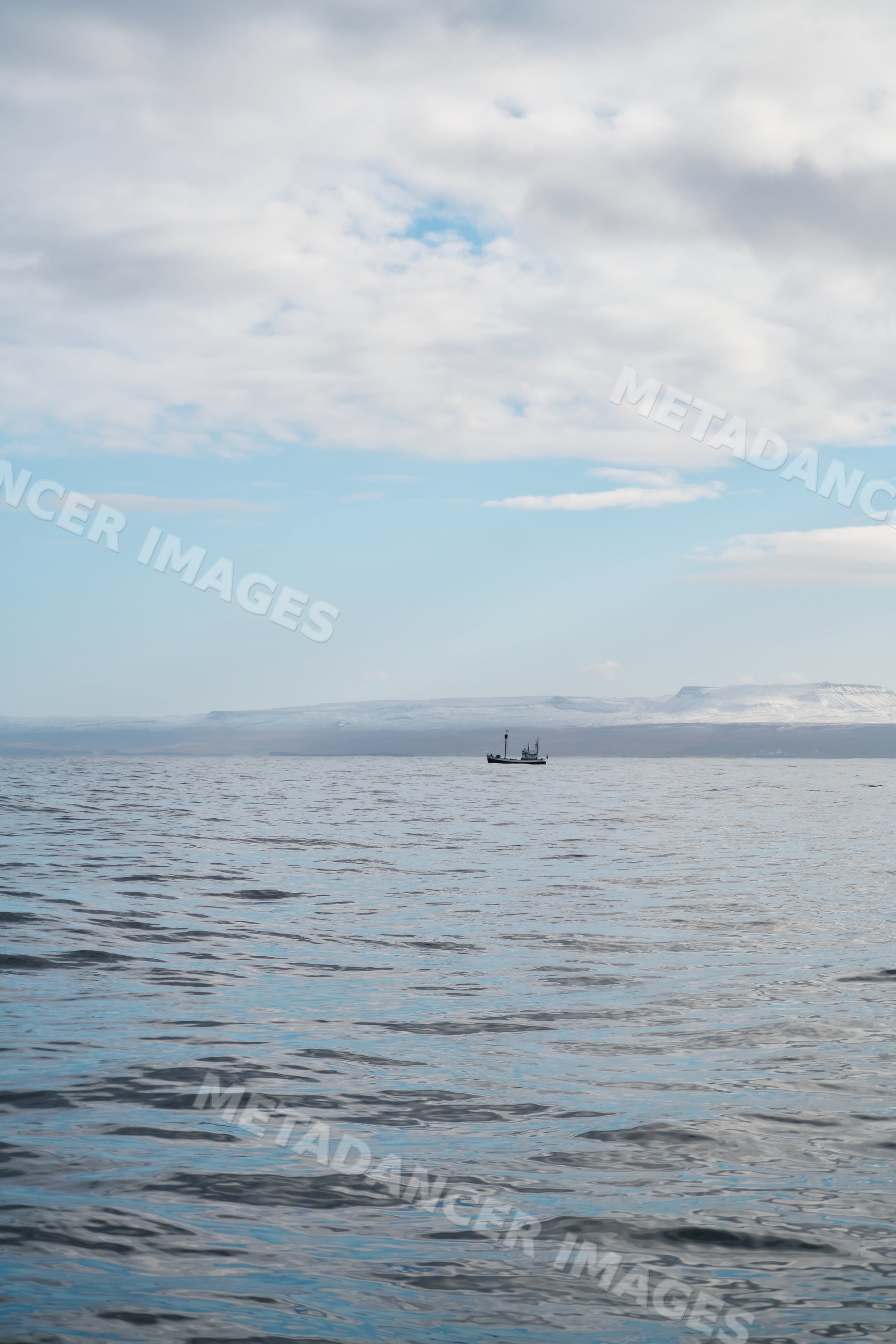 A fishing boat floats on calm waters with snowy hills