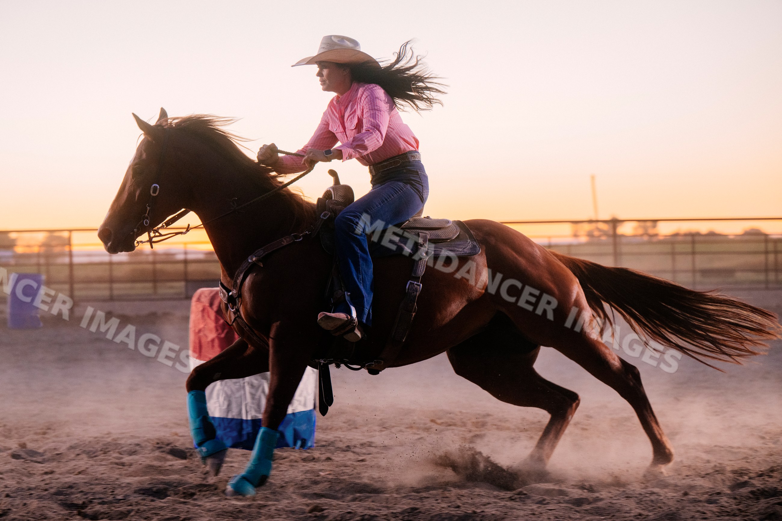 Cowgirl racing horse in barrel race at sunset outdoors