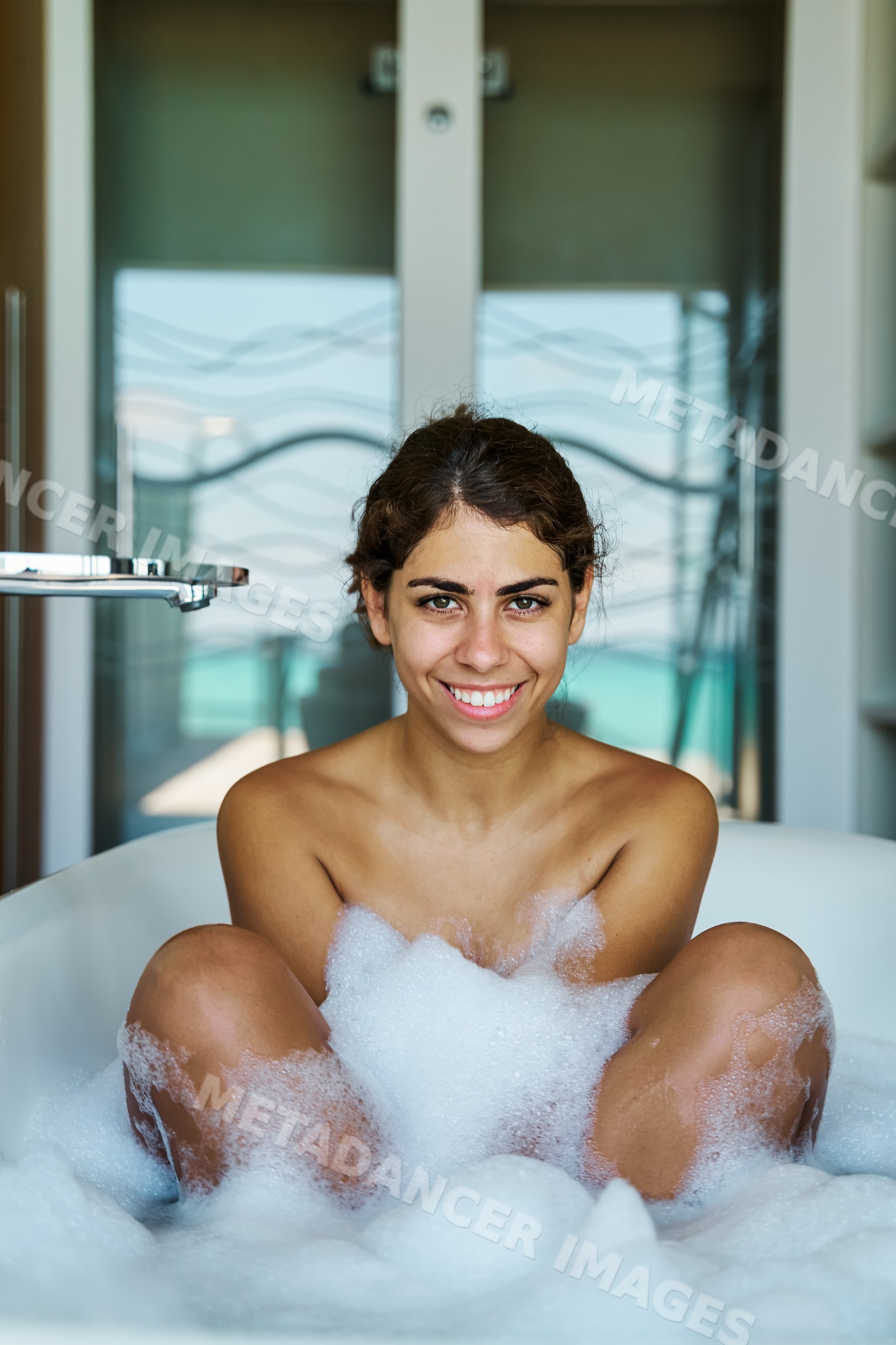 A young white woman enjoys a relaxing bubble bath in a bathroom