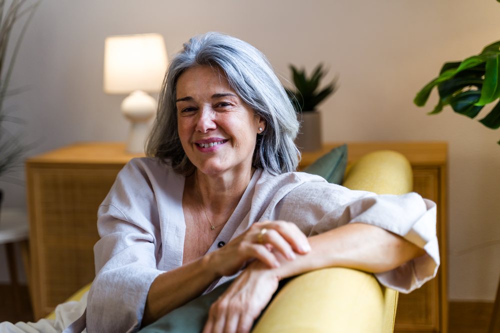 White woman with gray hair smiling on yellow sofa in living room