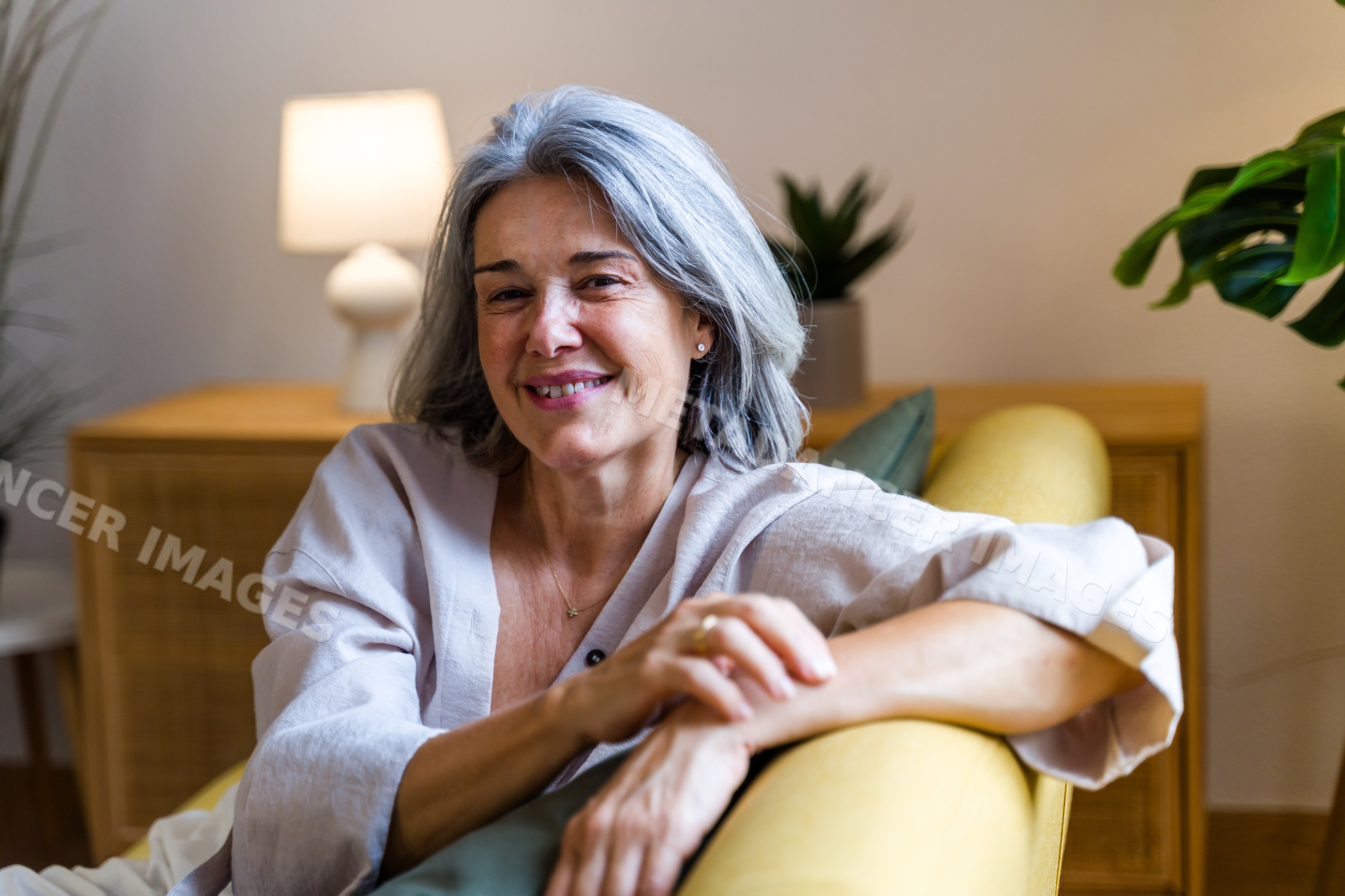 White woman with gray hair smiling on yellow sofa in living room