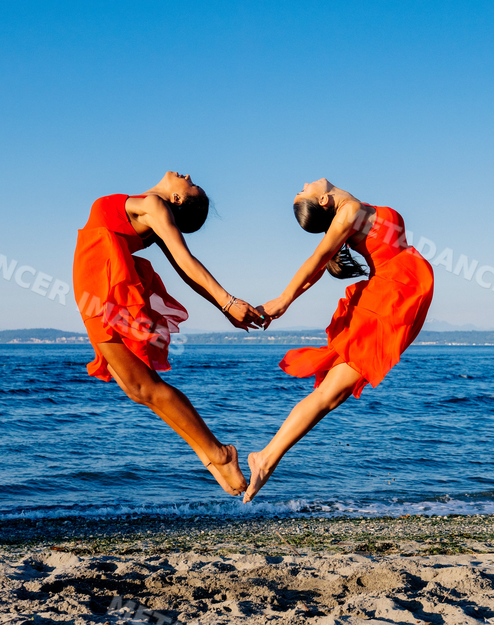 Two women in red dresses perform partner acrobatics jumping on a beach
