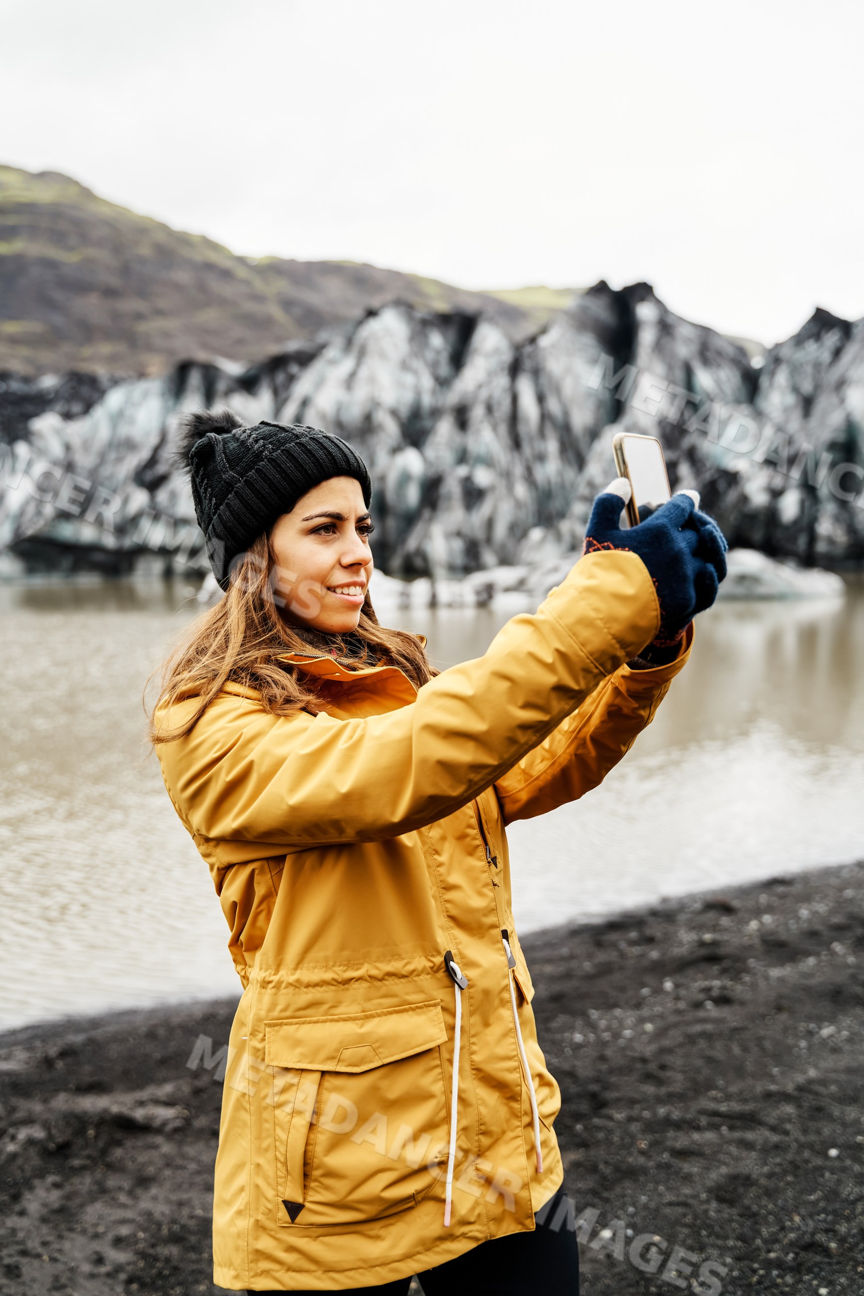 A white woman takes a photo at a glacier lake