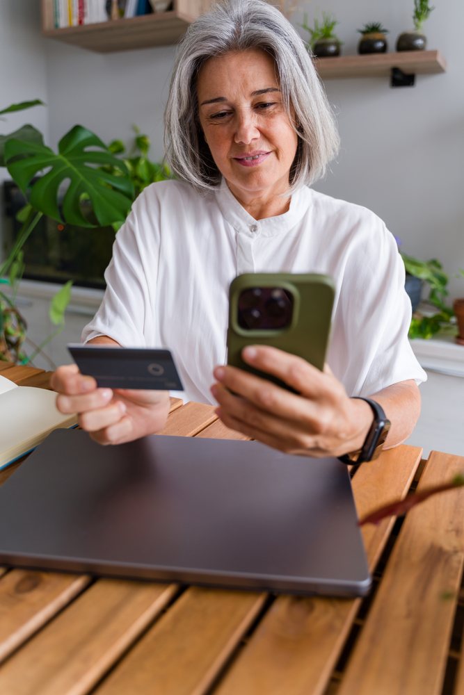 Mature white woman using smartphone and payment card for online