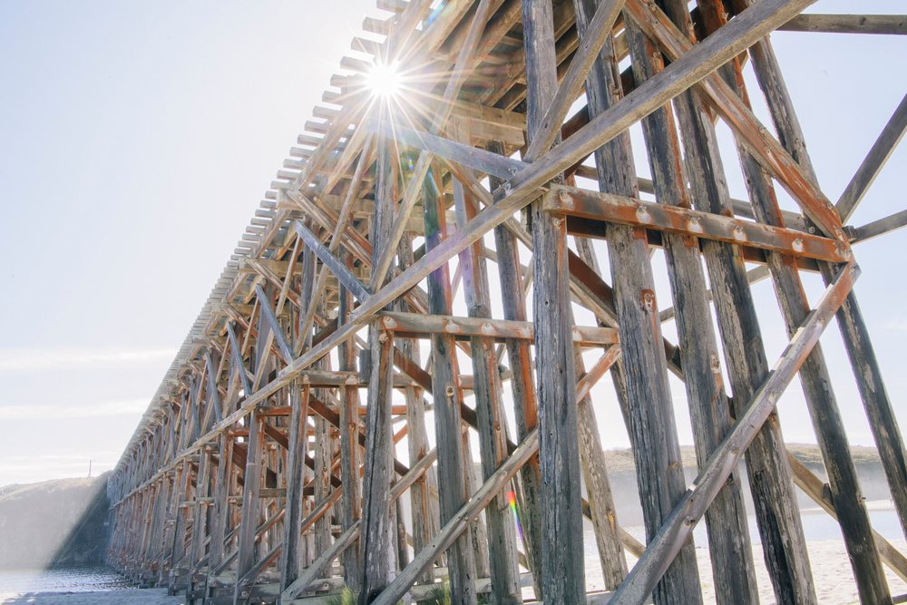 Weathered wooden bridge with sun flare over coastal water