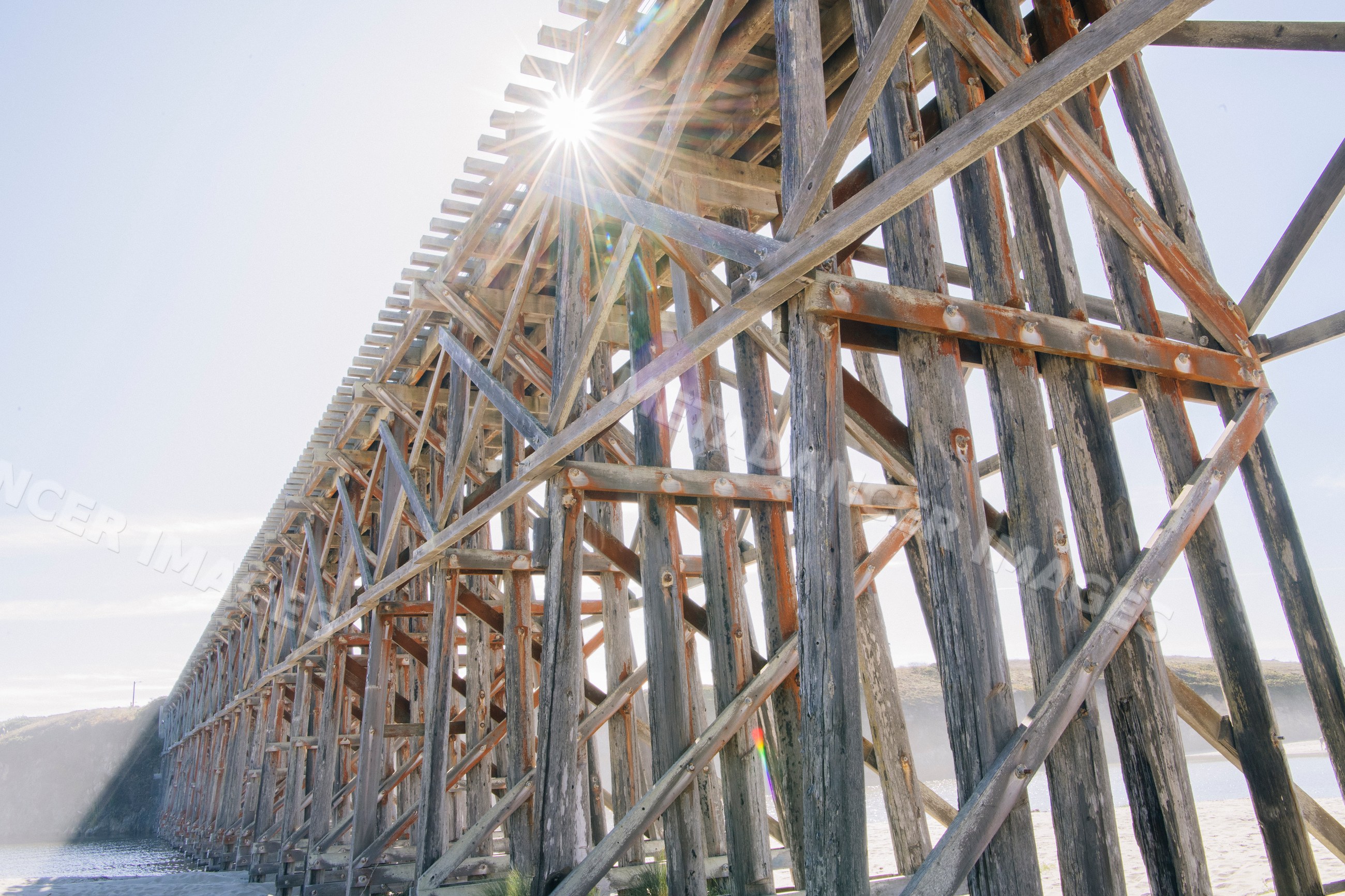 Weathered wooden bridge with sun flare over coastal water
