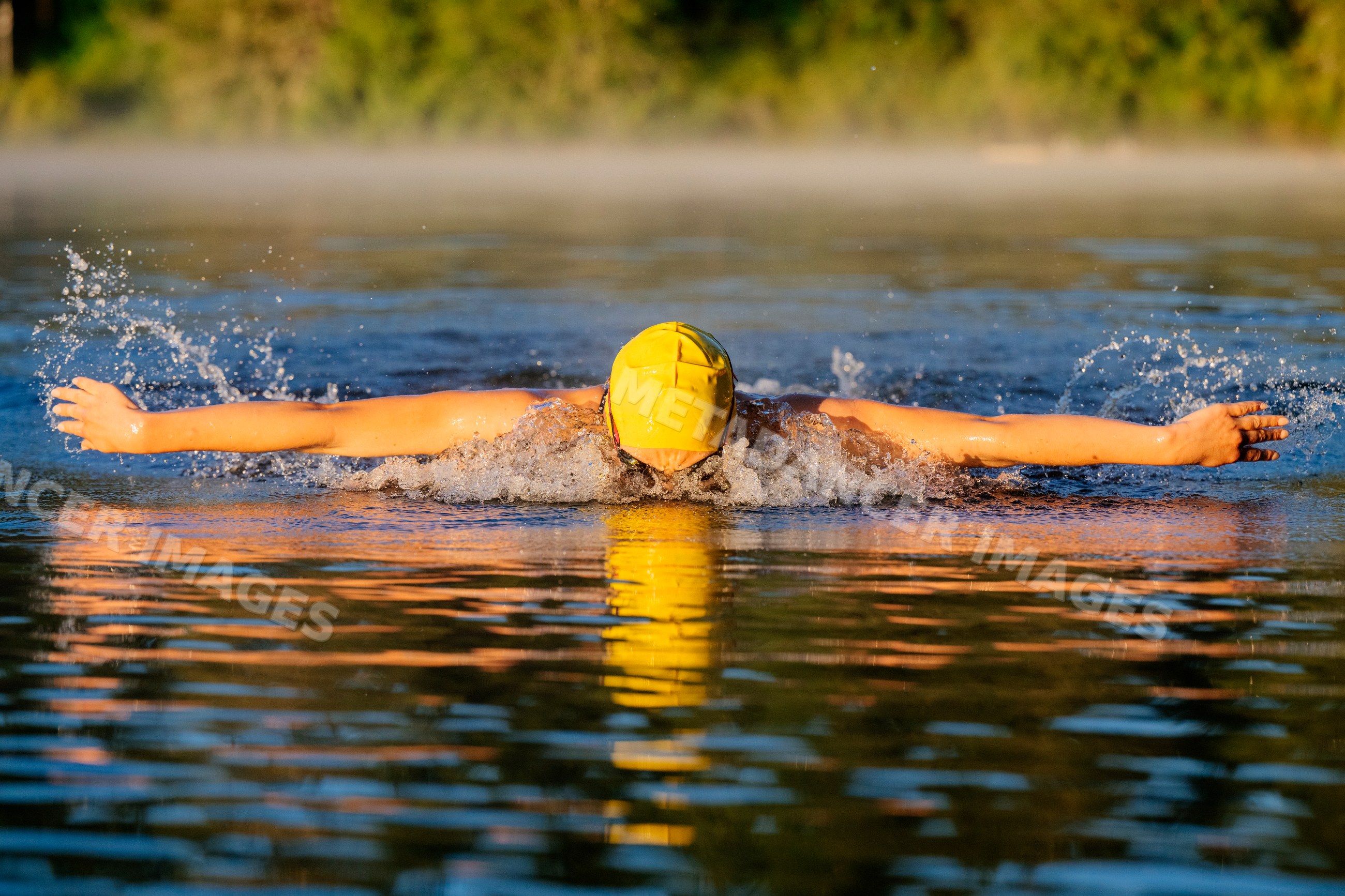 White swimmer performing butterfly stroke in open water at sunrise