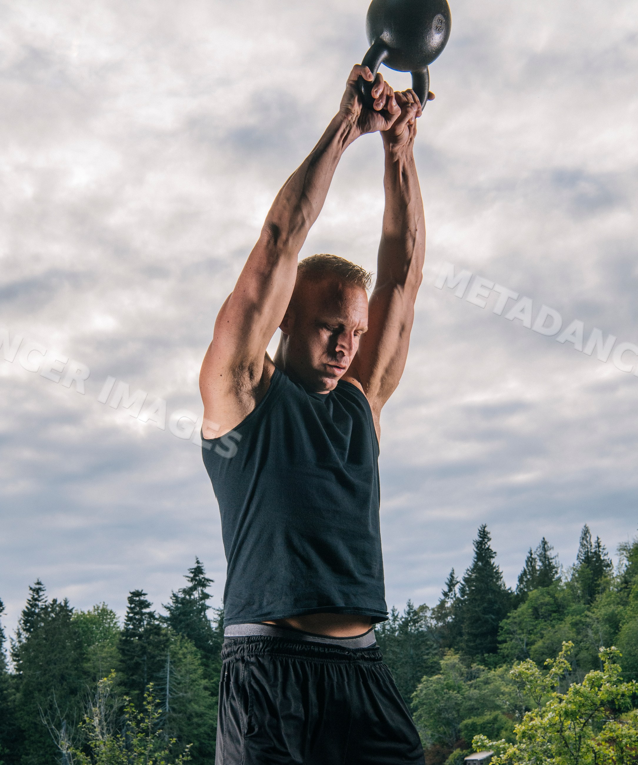 White man lifting kettlebell overhead during outdoor workout