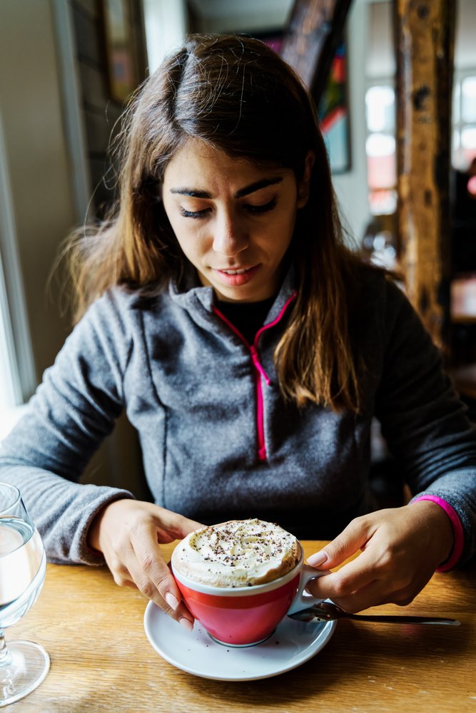 A white woman holds a cup of whipped cream coffee in a cafe in Iceland