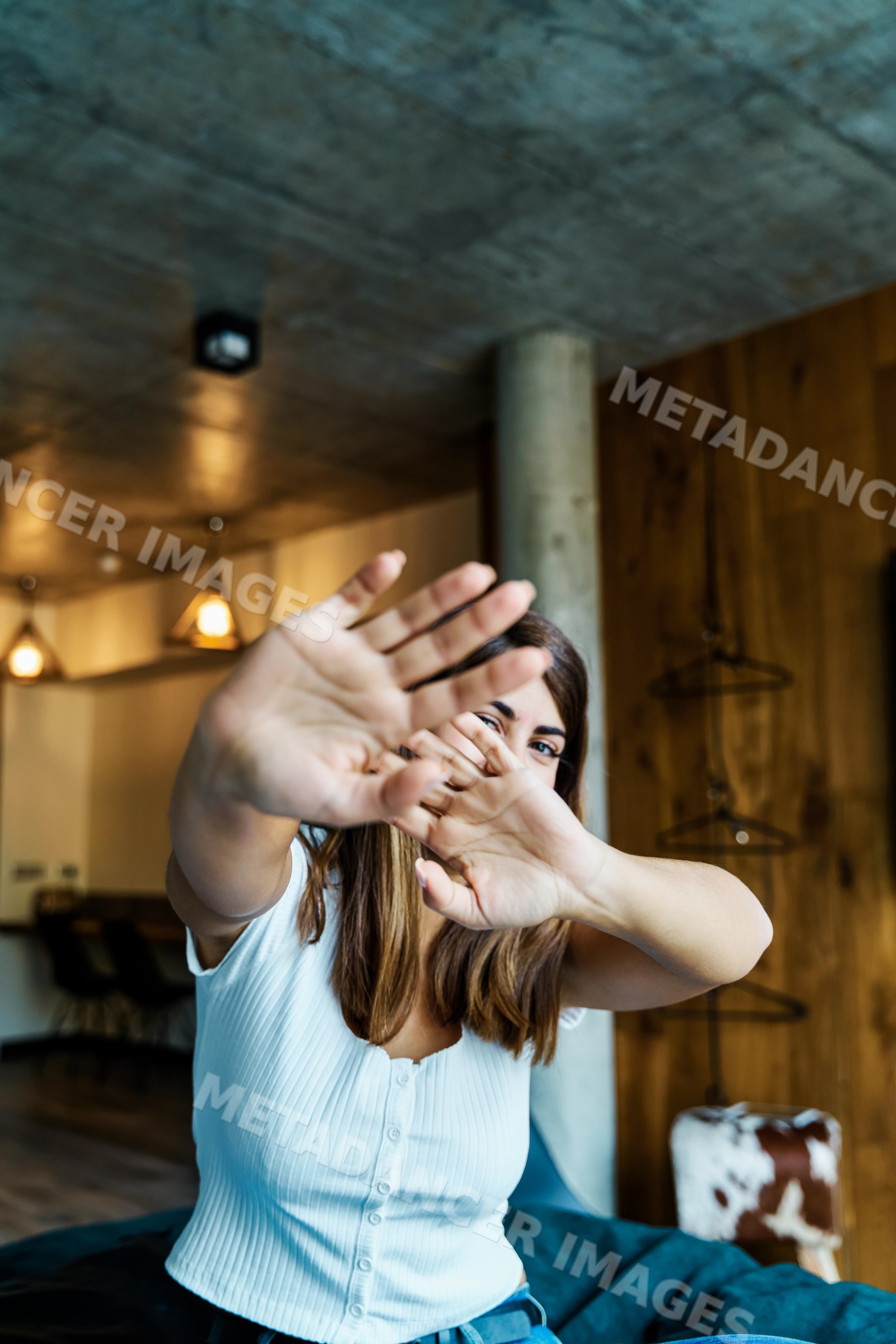 A woman playfully covers her face inside a modern cozy room in a hotel