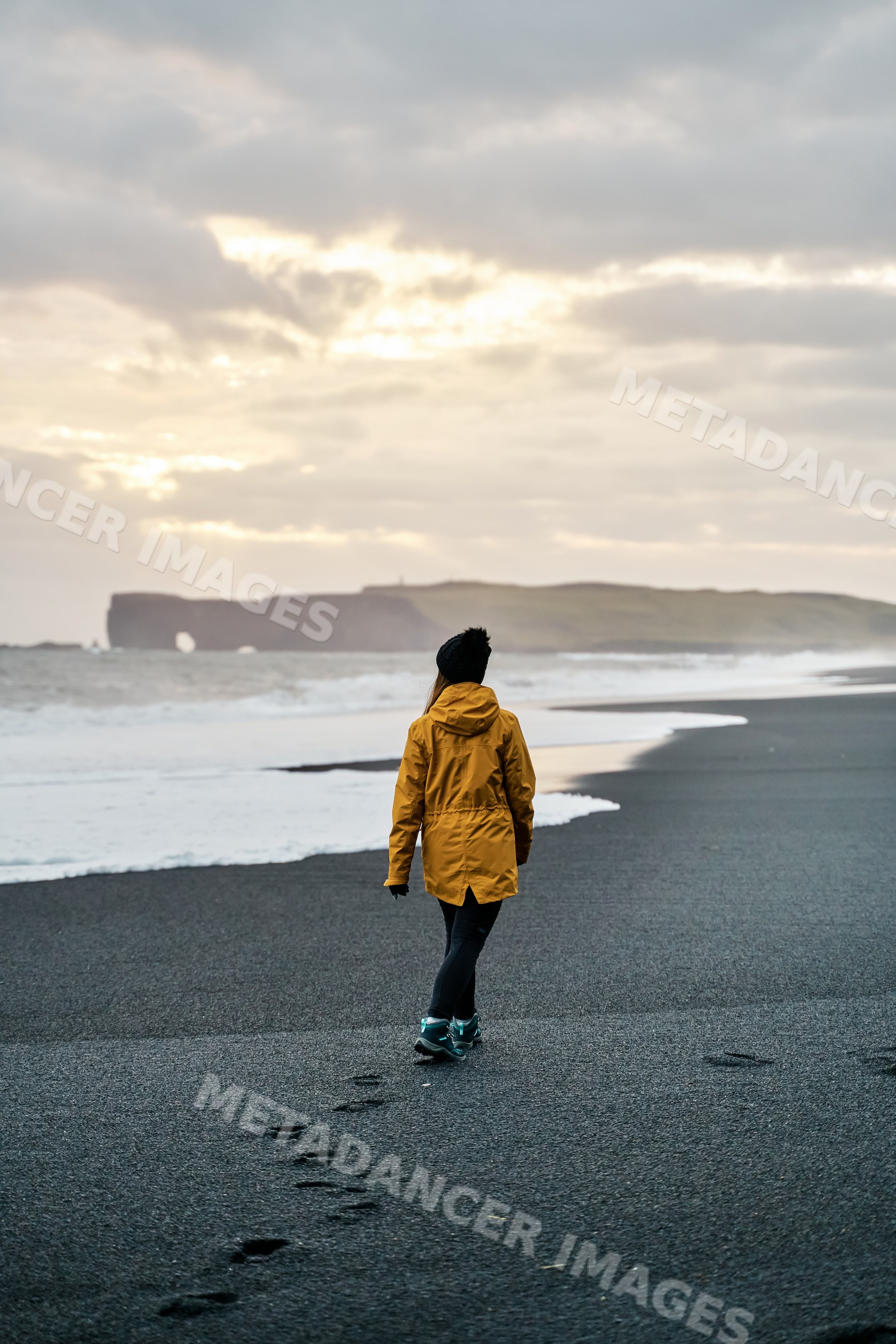 White Person walking on a black sand beach by the ocean in a beach