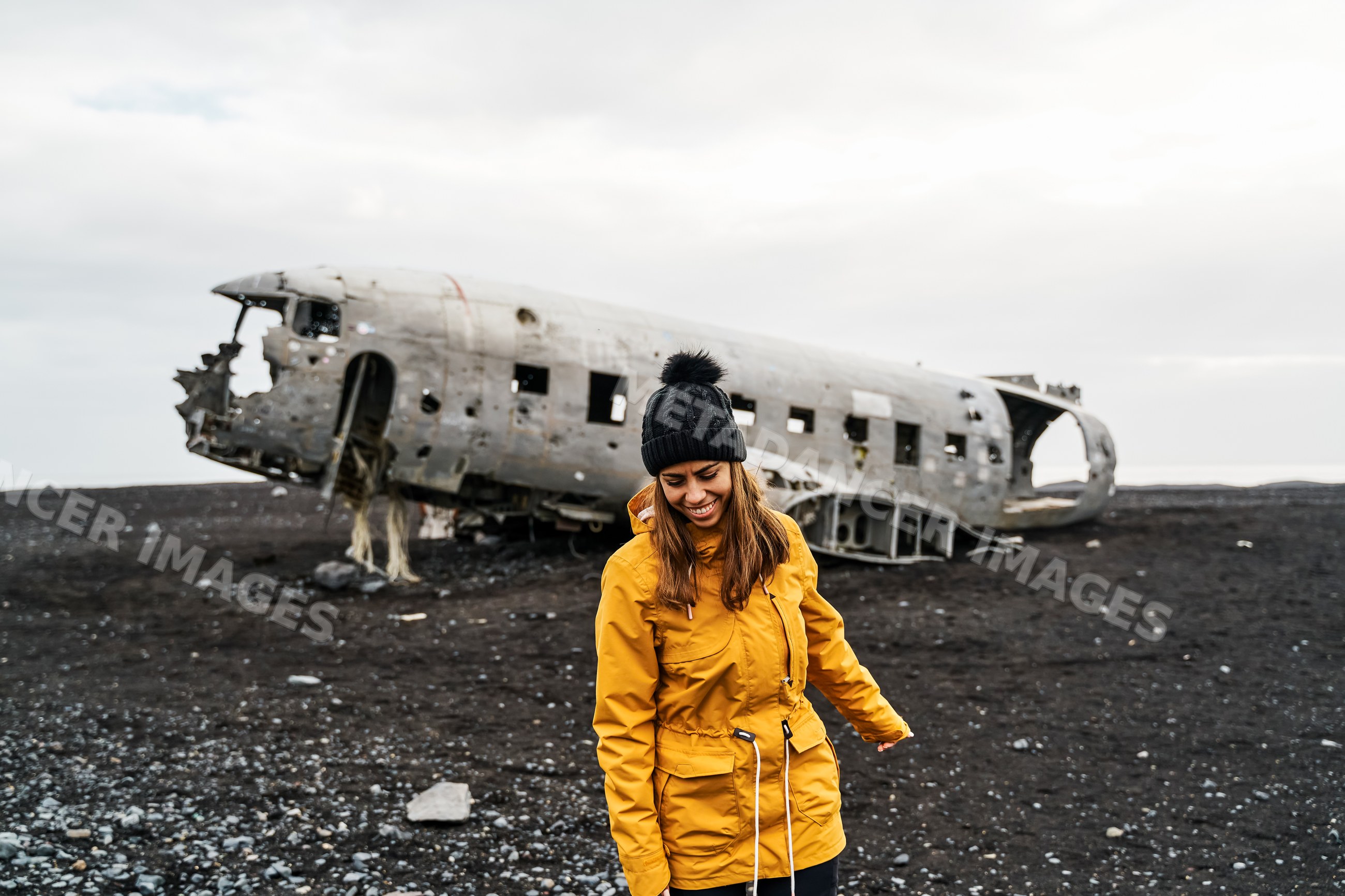 A white woman smiles in front of an abandoned airplane wreck