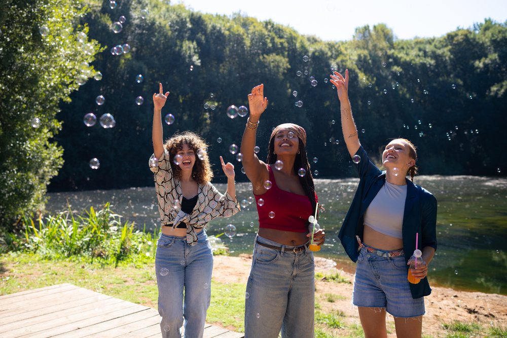 Three white and African American women blowing bubbles outdoors