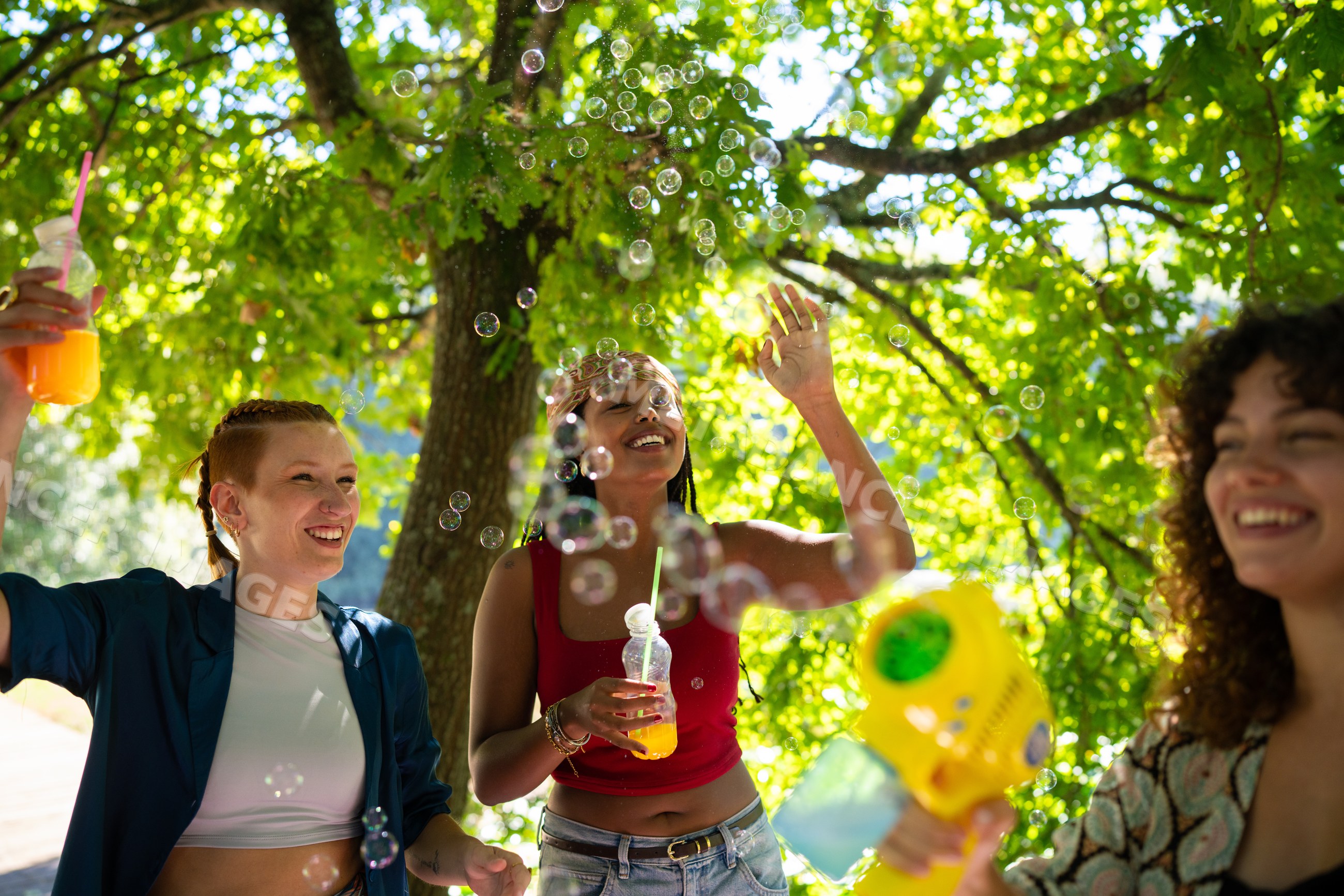 White and African American women enjoying bubbles outdoors under green