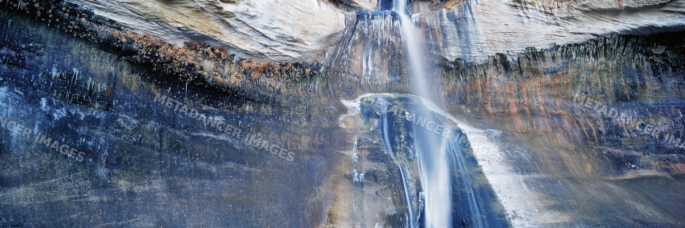 Waterfall cascading on layered sedimentary rock cliff