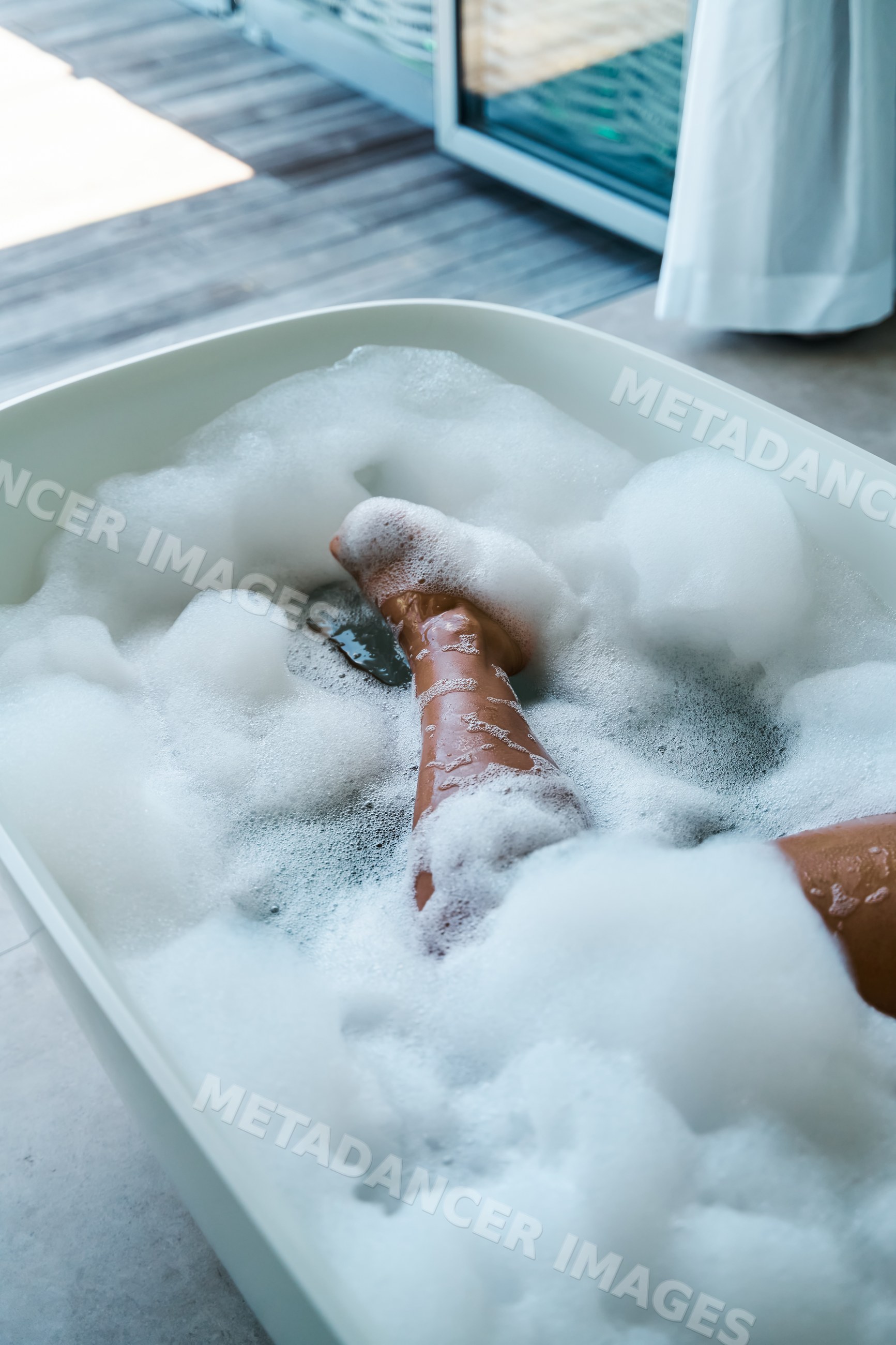 A white person relaxing with legs in a bubble bath inside a bathtub