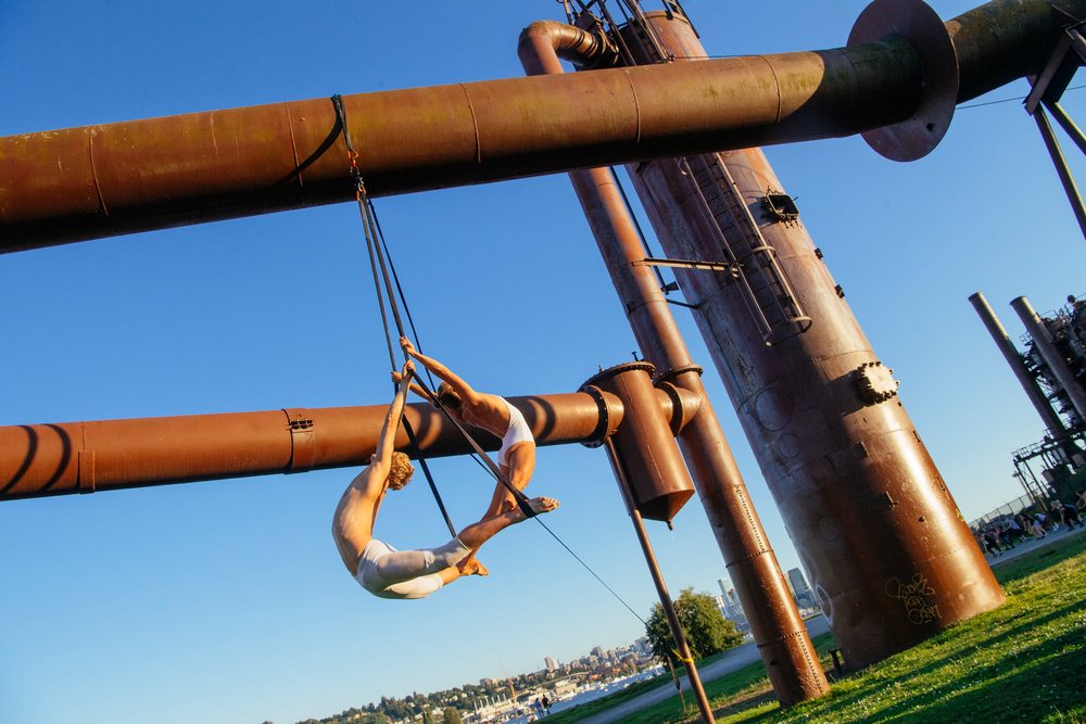 Two aerialists performing trapeze act on steel structure outdoors